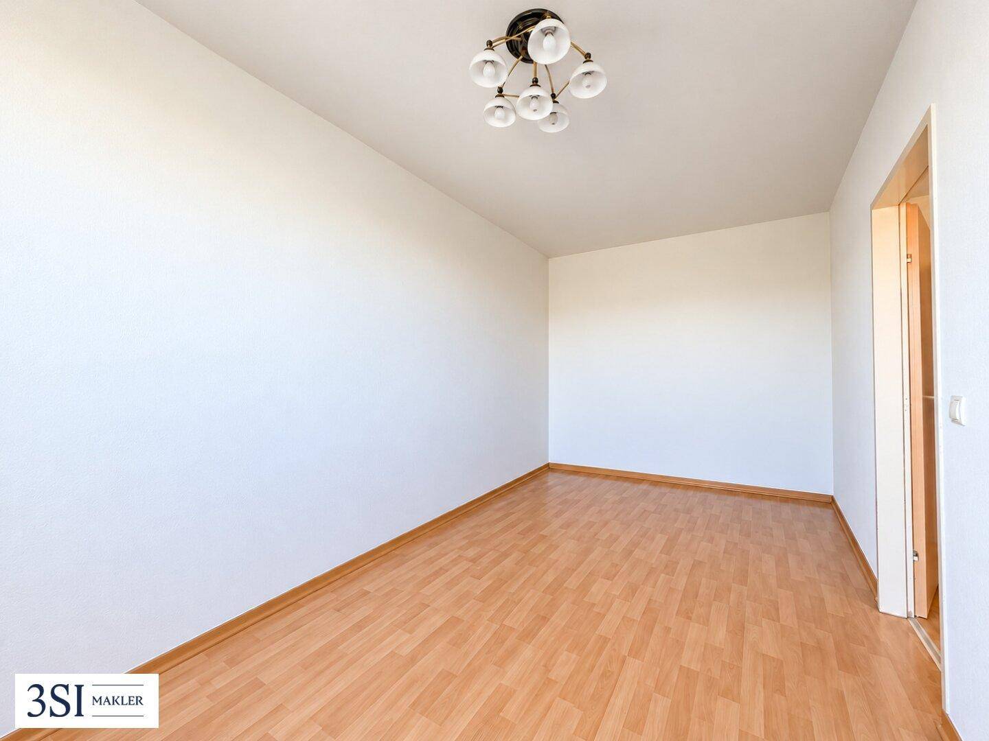 Leeres Zimmer mit hellem Parkettboden und weißen Wänden, bereit zur individuellen Einrichtung.