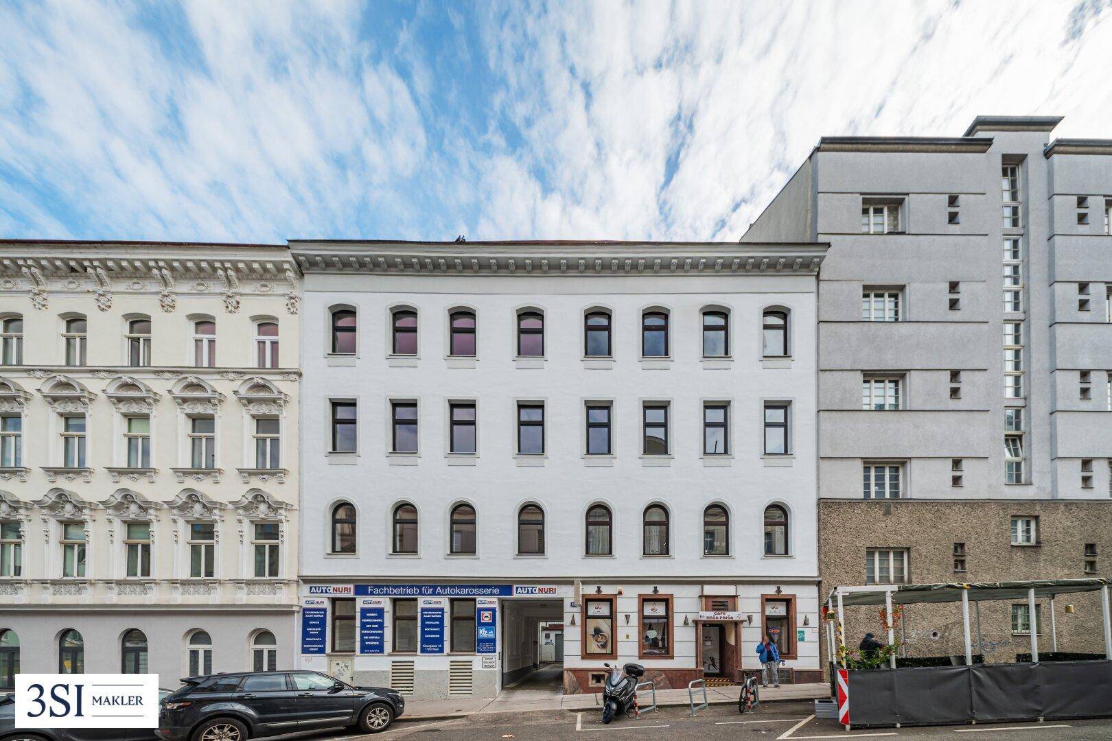 Historisches Gebäude mit weißer Fassade, vielen Fenstern und Geschäften im Erdgeschoss.