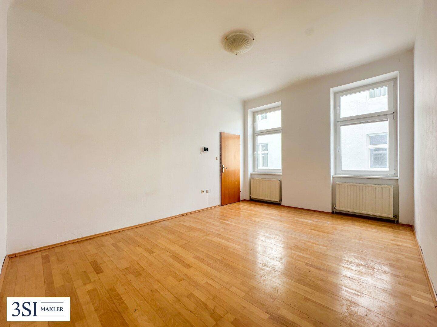 Geräumiges, leeres Zimmer mit Holzboden und zwei großen Fenstern, bereit zur individuellen Gestaltung.
