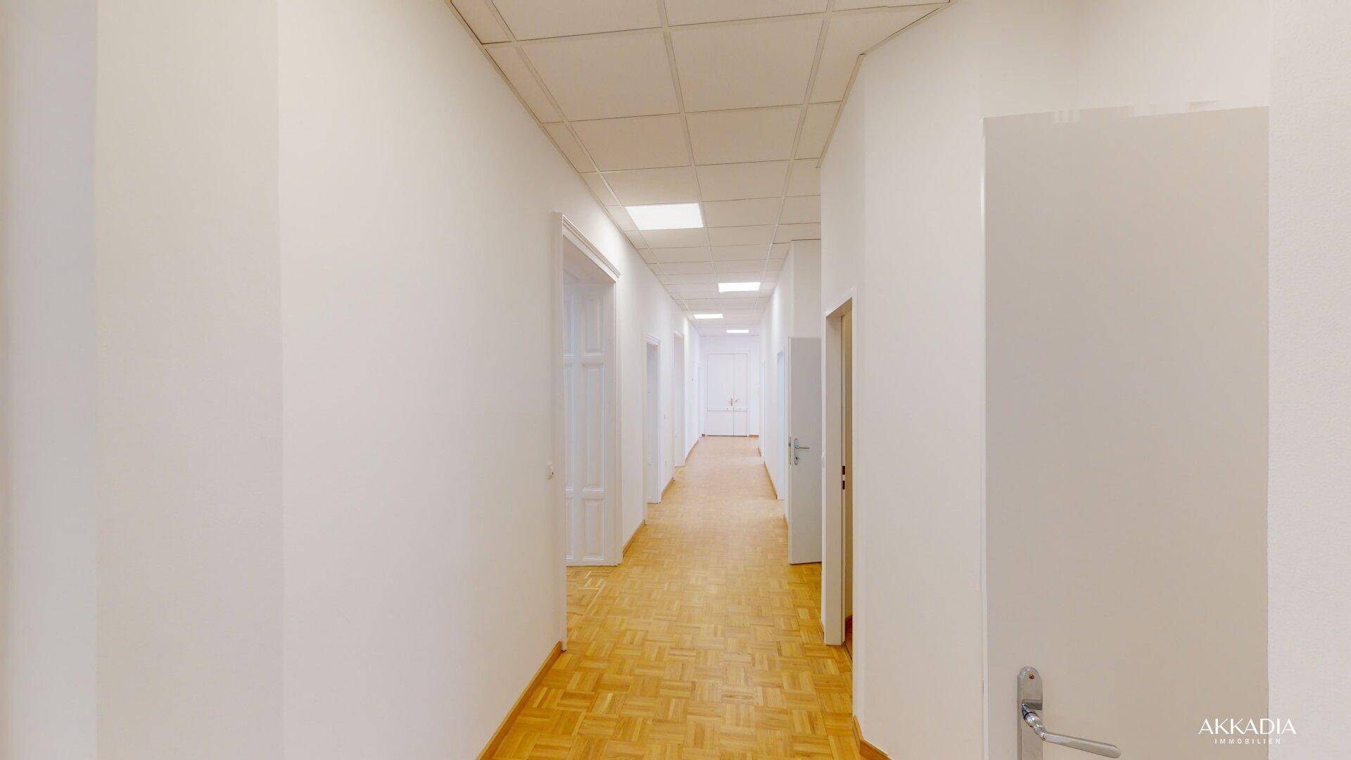 Langer, heller Flur mit Parkettboden, weißen Wänden und Deckenbeleuchtung in einem gepflegten Zustand.