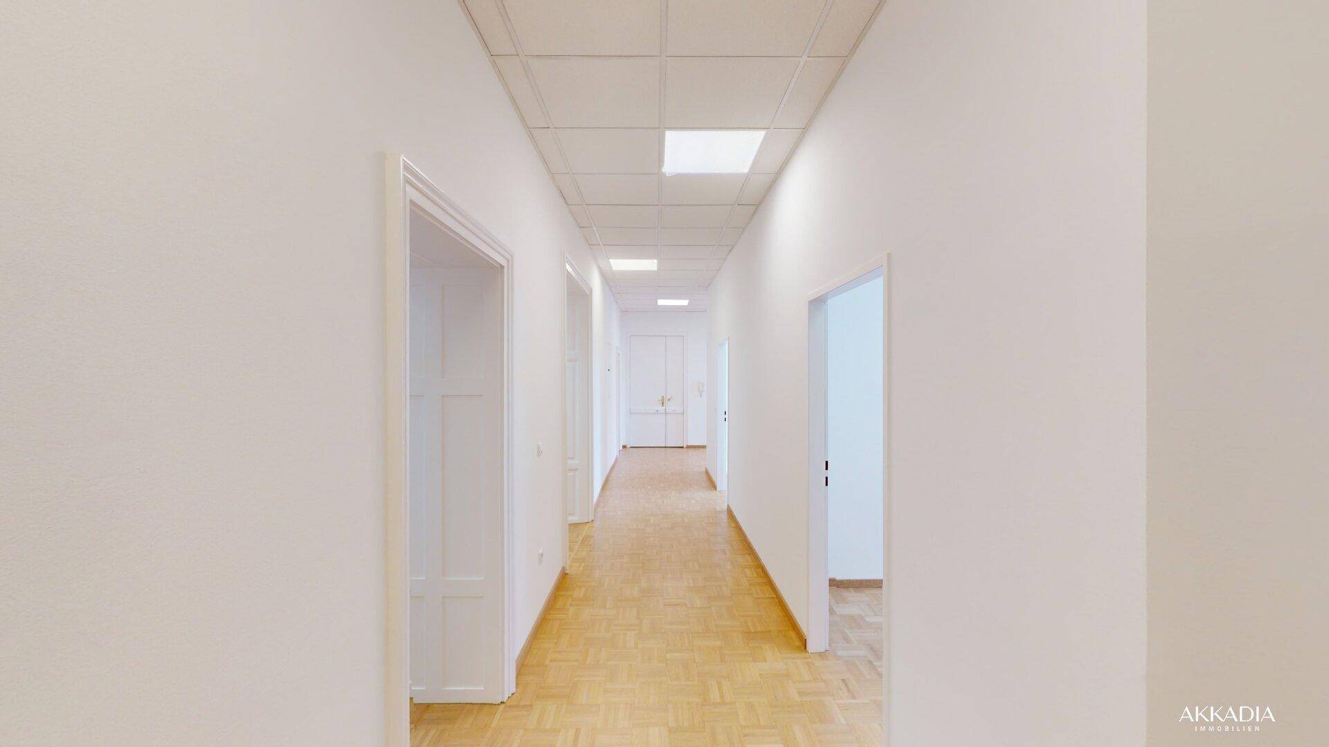 Langer, heller Flur mit Parkettboden, weißen Wänden und Deckenbeleuchtung in einem gepflegten Zustand.