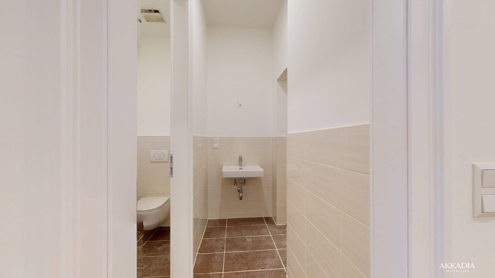Modernes Gäste-WC mit Wand-WC, kleinem Waschbecken und hellen Fliesen.