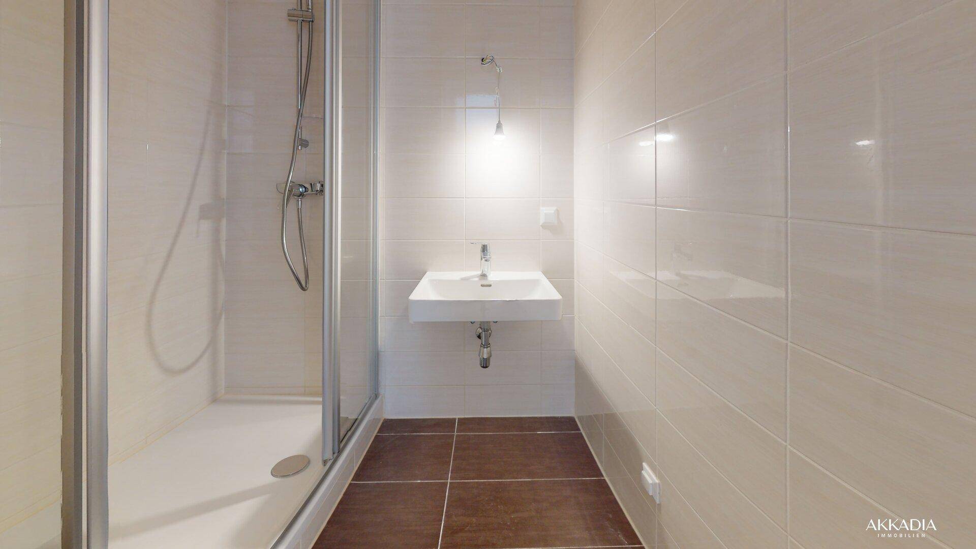 Modernes Badezimmer mit Duschkabine, Waschbecken und hellen Wand- und Bodenfliesen.