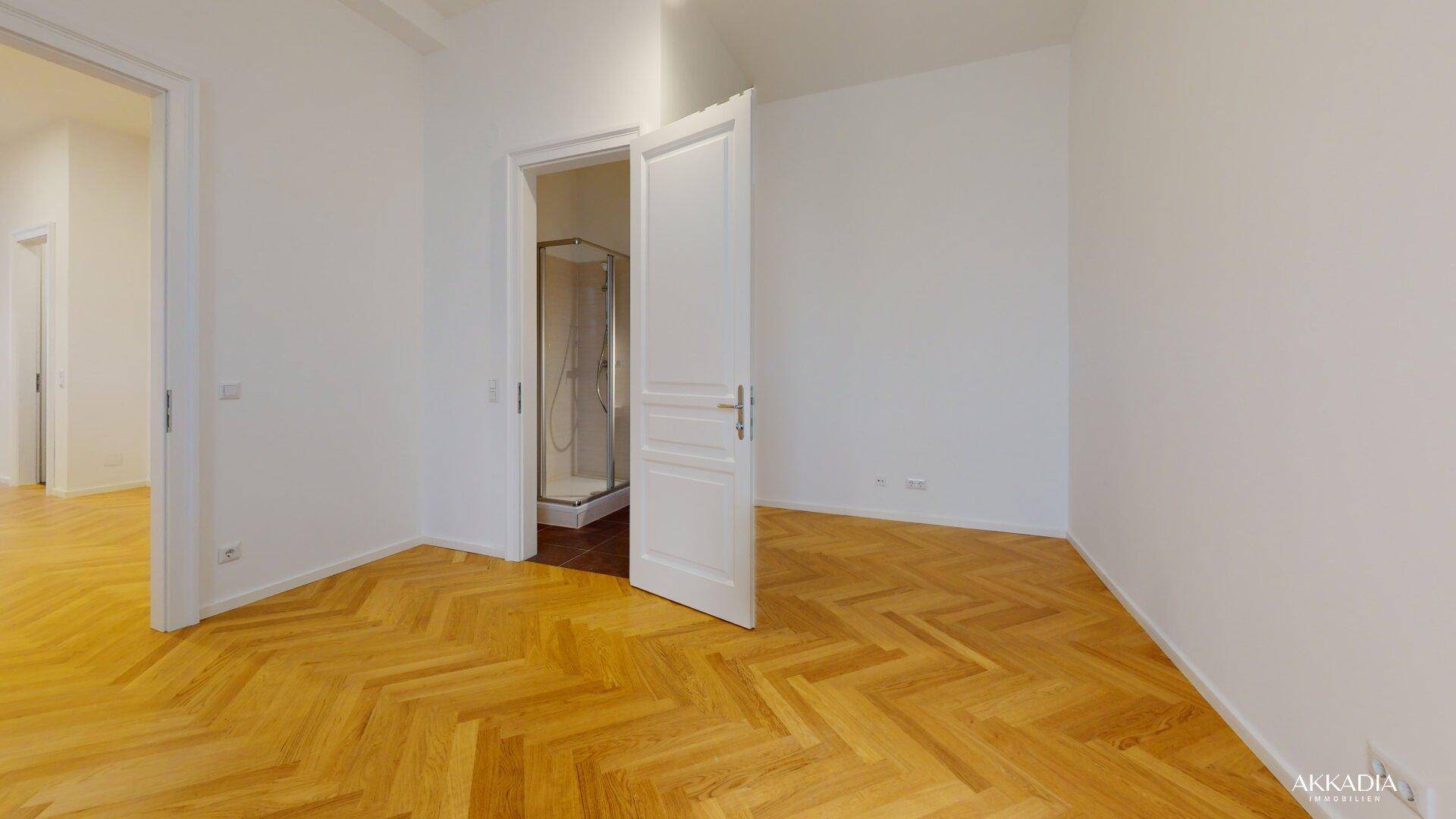 Helles Zimmer mit Fischgrätparkett und Zugang zu einem modernen Badezimmer.