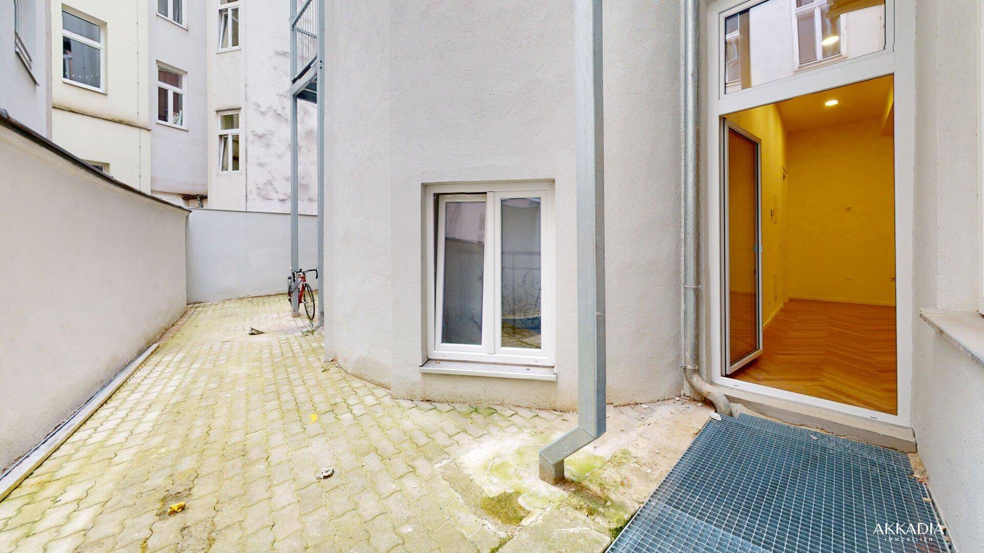 Kleiner, gepflasterter Innenhof mit Zugang zu einem gelb gestrichenen Raum.