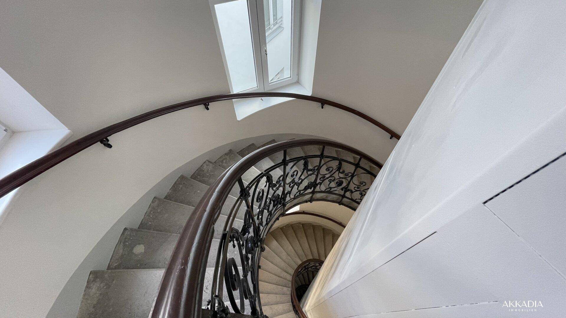 Geschwungene Treppe mit schmiedeeisernem Geländer und Oberlicht für natürliches Licht.
