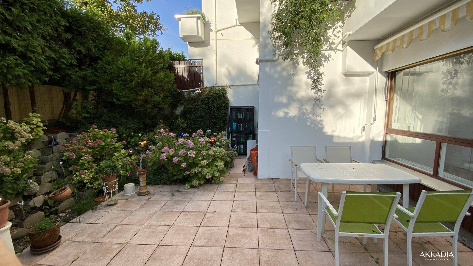 Sonniger Terrassenbereich mit Gartenmöbeln und üppiger grüner Bepflanzung.