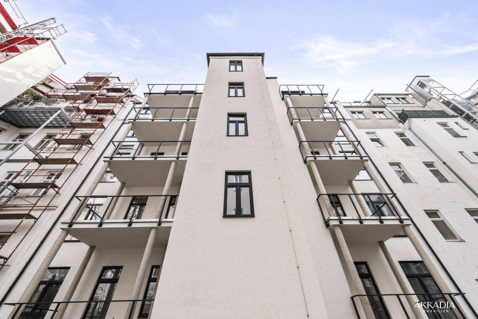 Vertikale Ansicht einer modernen Gebäudefassade mit Balkonen und Gerüst an der Seite.