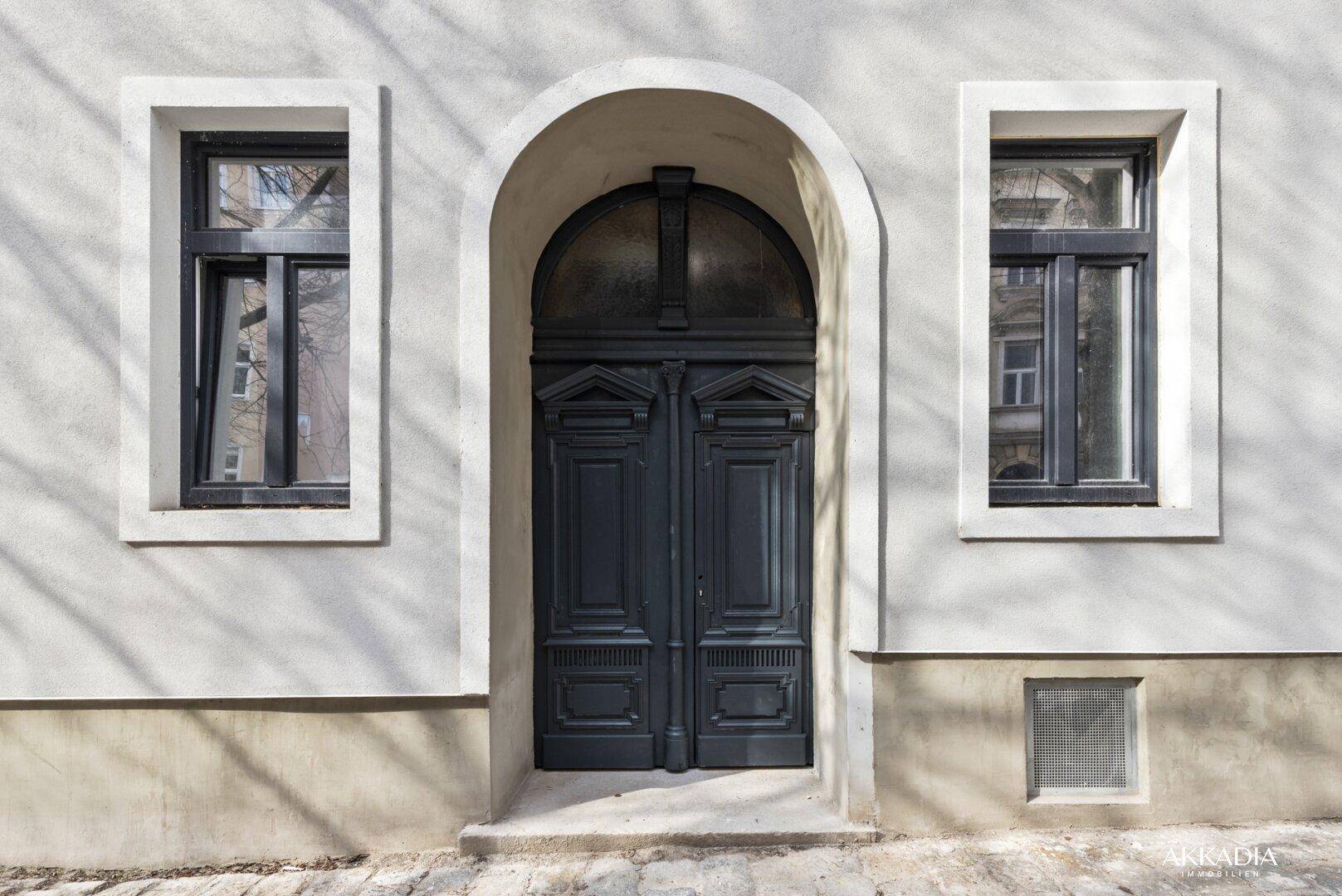 Historischer Hauseingang mit großer Holztür und zwei Fenstern in der Fassade.
