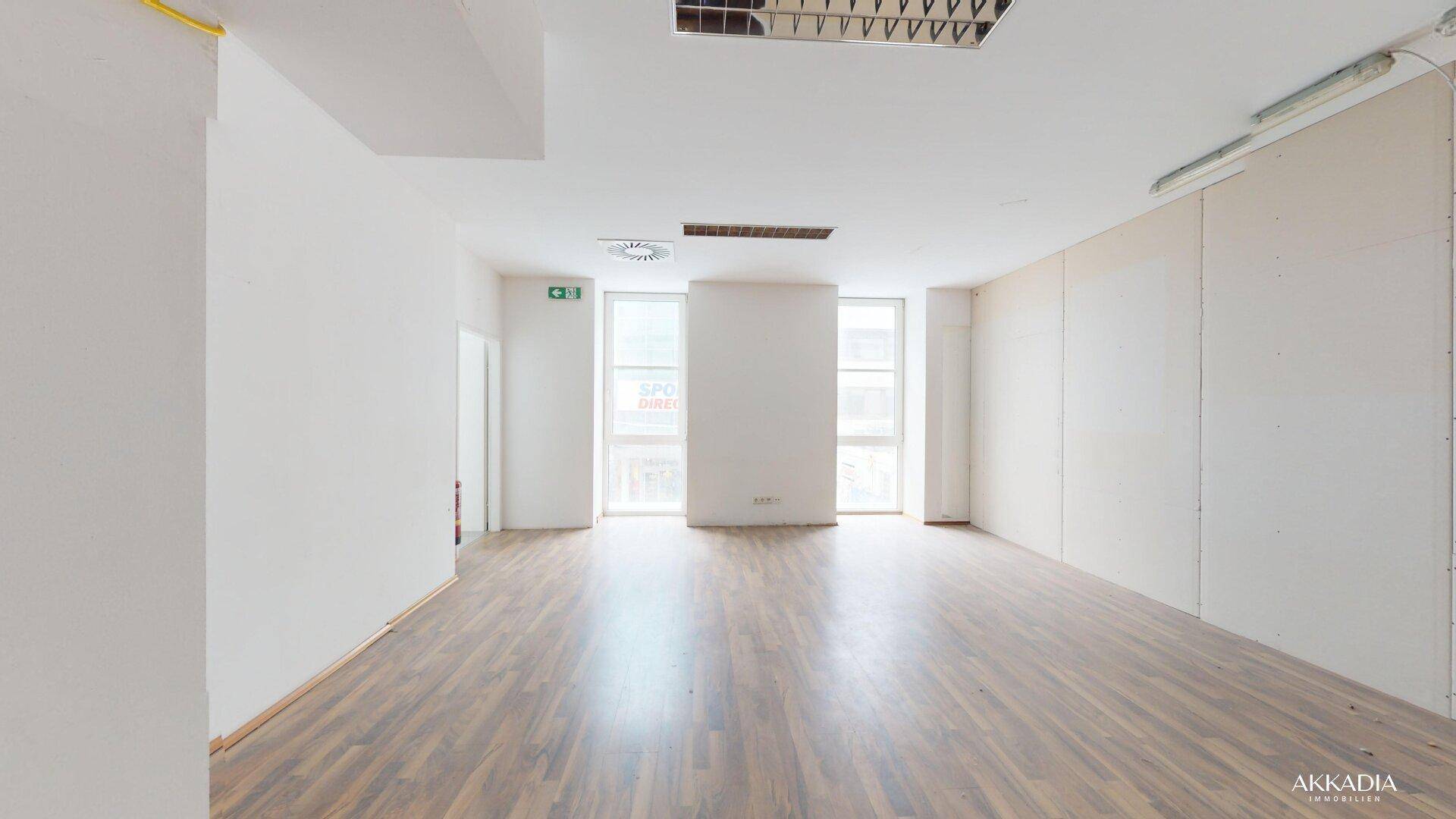 Großer, heller Büroraum mit hohen Fenstern und Laminatboden, bietet viel Tageslicht.