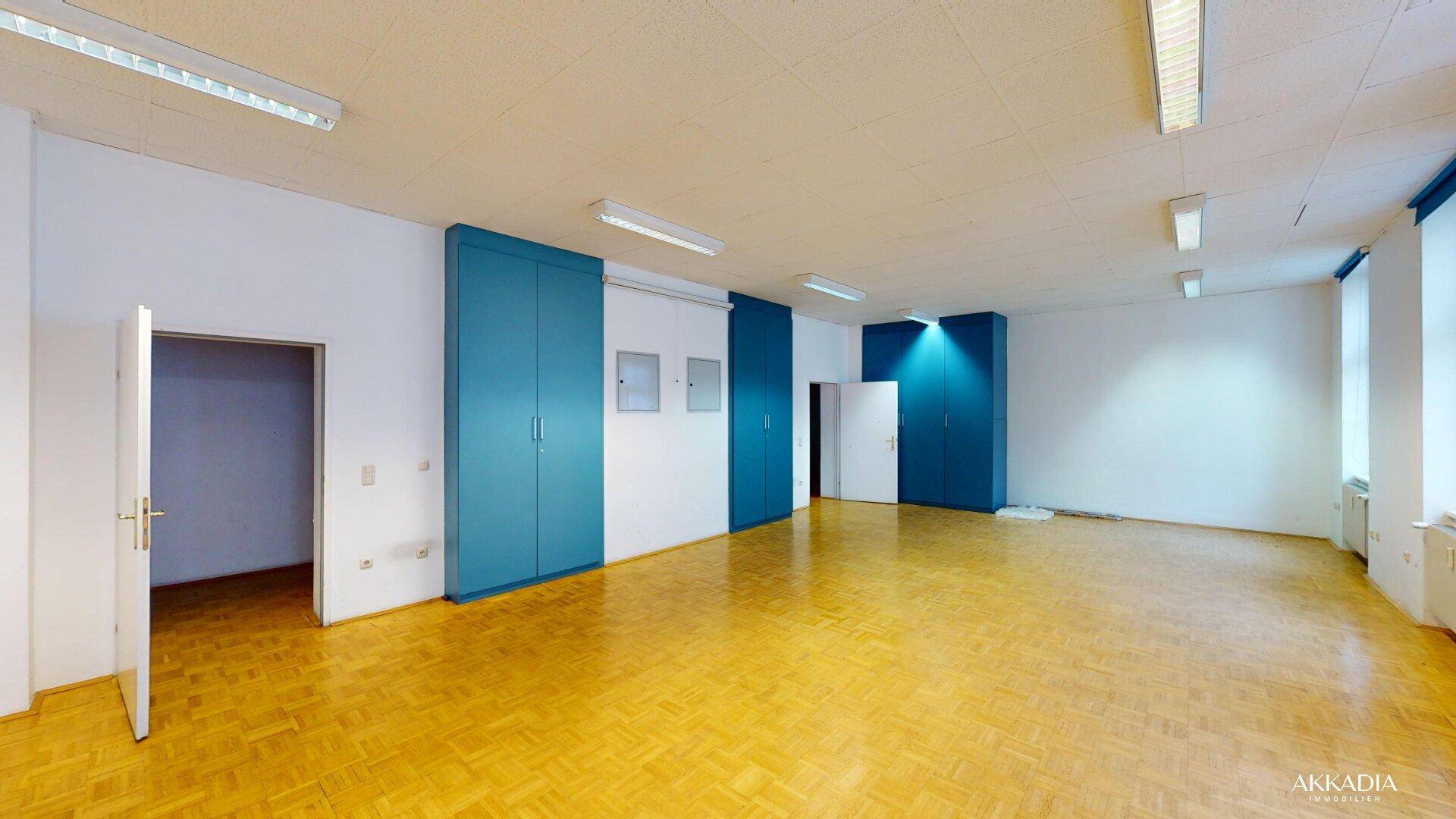 Großer Raum mit blauen Einbauschränken, Parkettboden und mehreren Türen, bietet viel Stauraum.