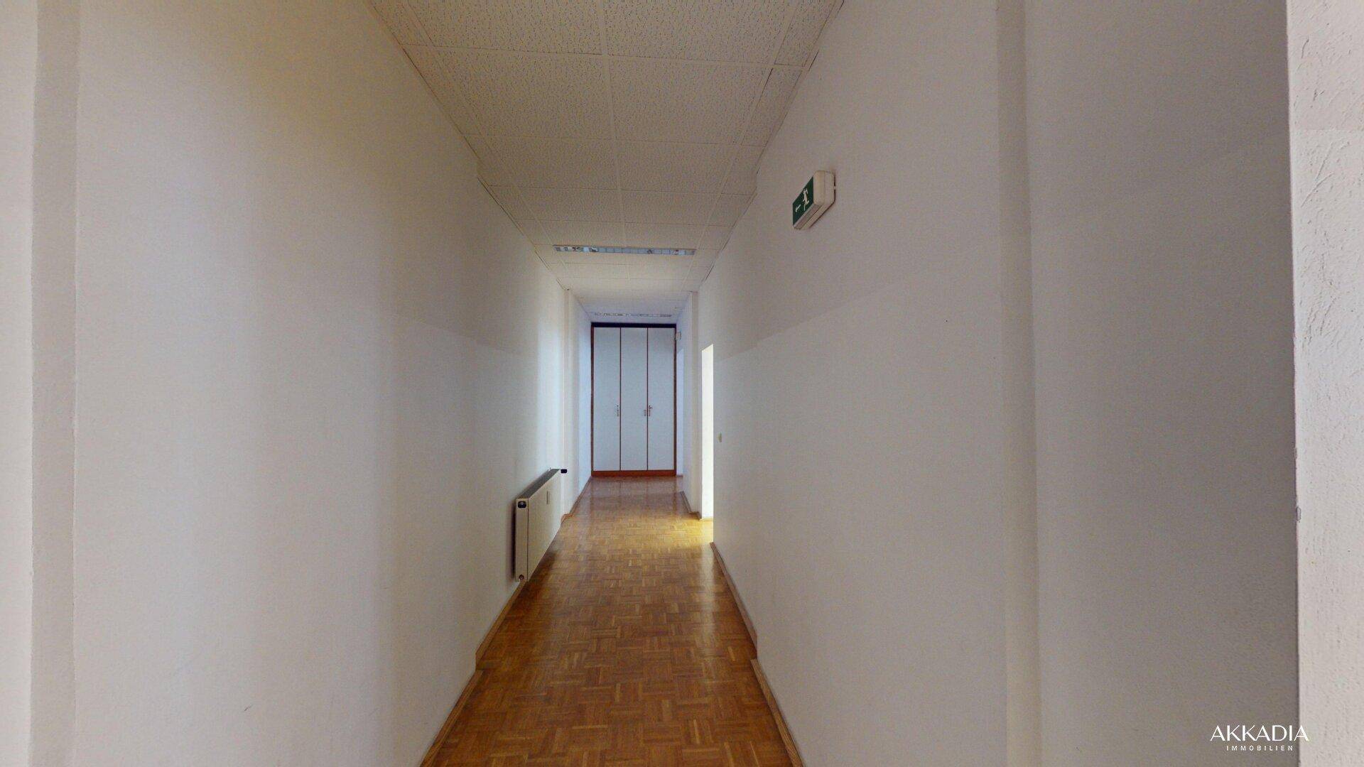 Langer, heller Flur mit Parkettboden und weißen Wänden, führt zu weiteren Räumen im Gebäude.