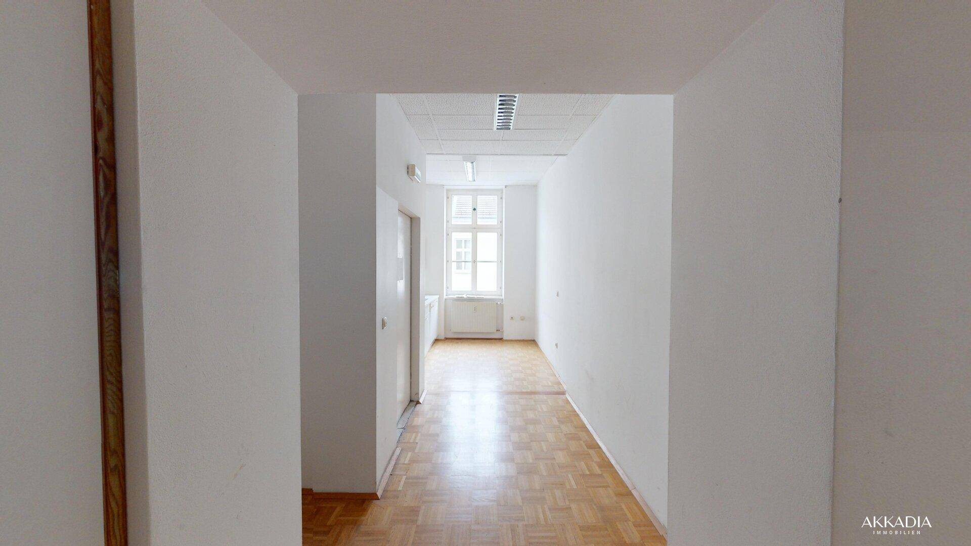 Heller Flur mit Parkettboden, der in einen weiteren Raum mit Fenster und Tageslicht führt.