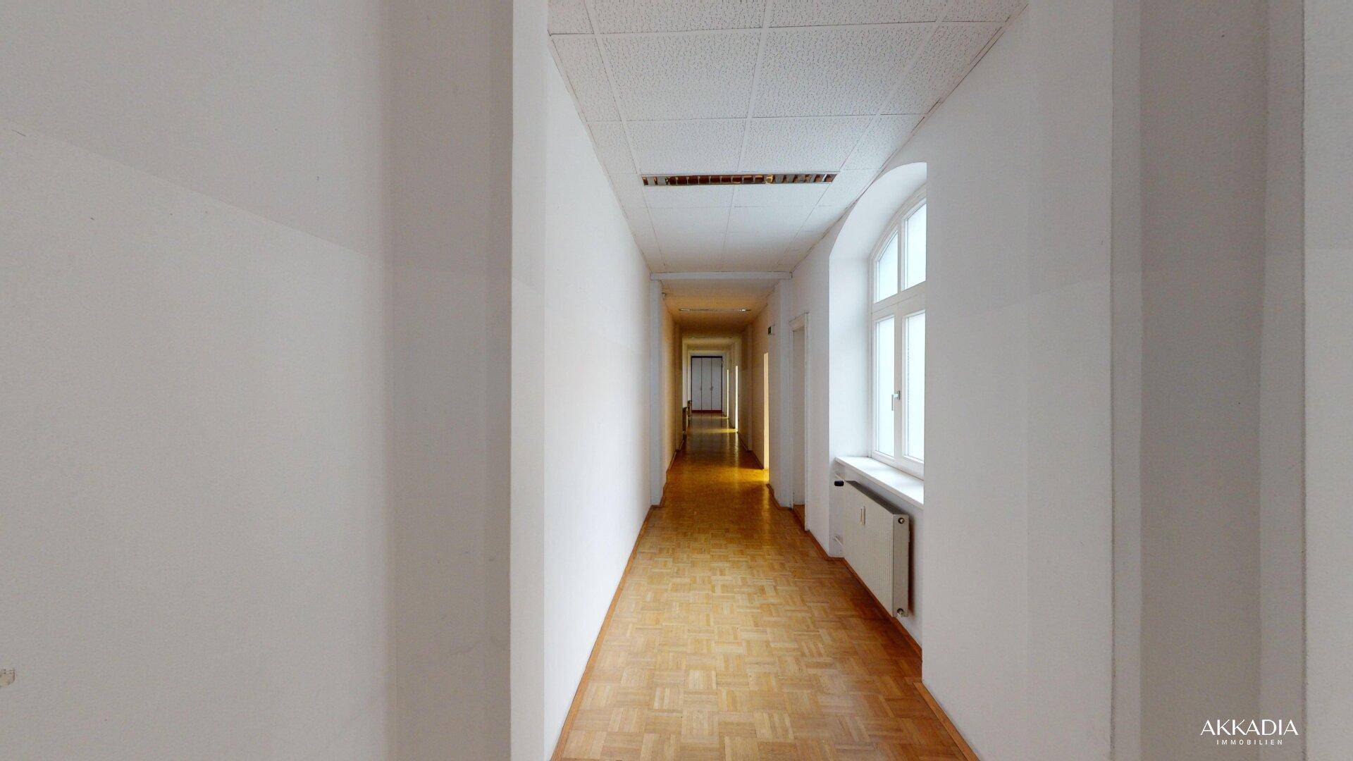Heller Flur mit Parkettboden und einem Fenster, das natürliches Licht in den Gang bringt.
