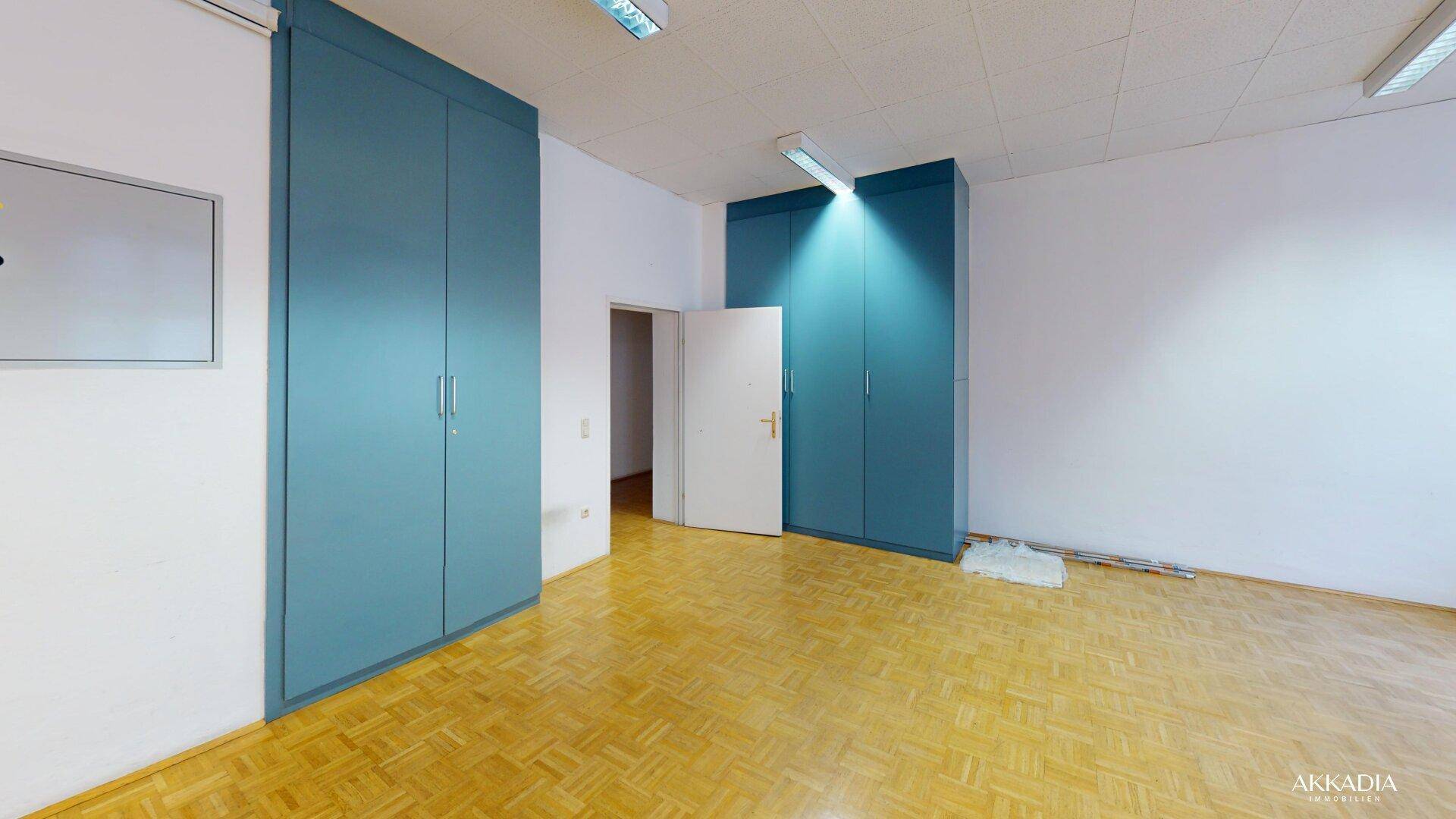 Heller Raum mit Parkettboden und blauen Einbauschränken, die zusätzlichen Stauraum bieten.