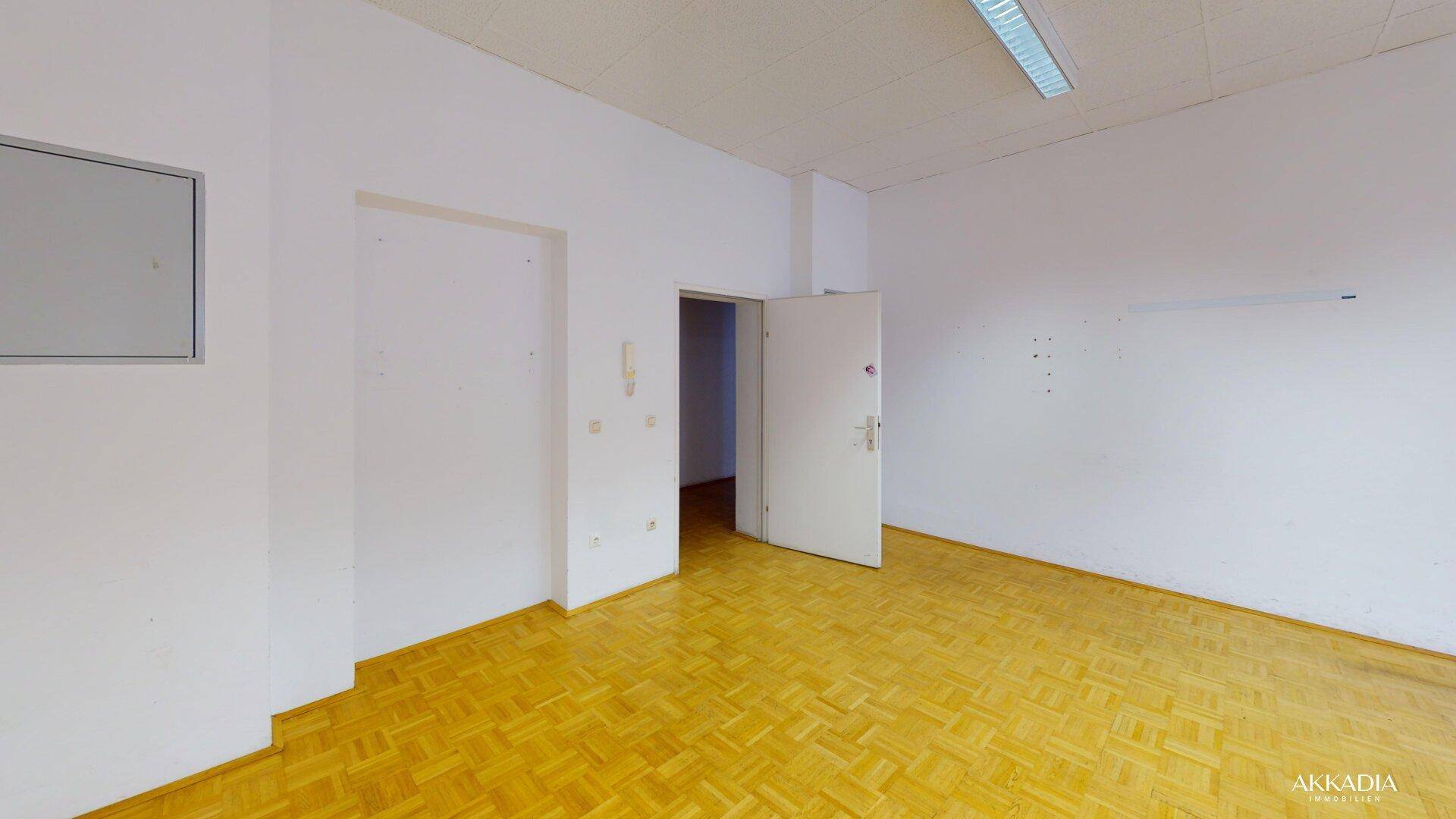 Heller Raum mit Parkettboden und einer Tür, die zu einem weiteren Bereich des Gebäudes führt.