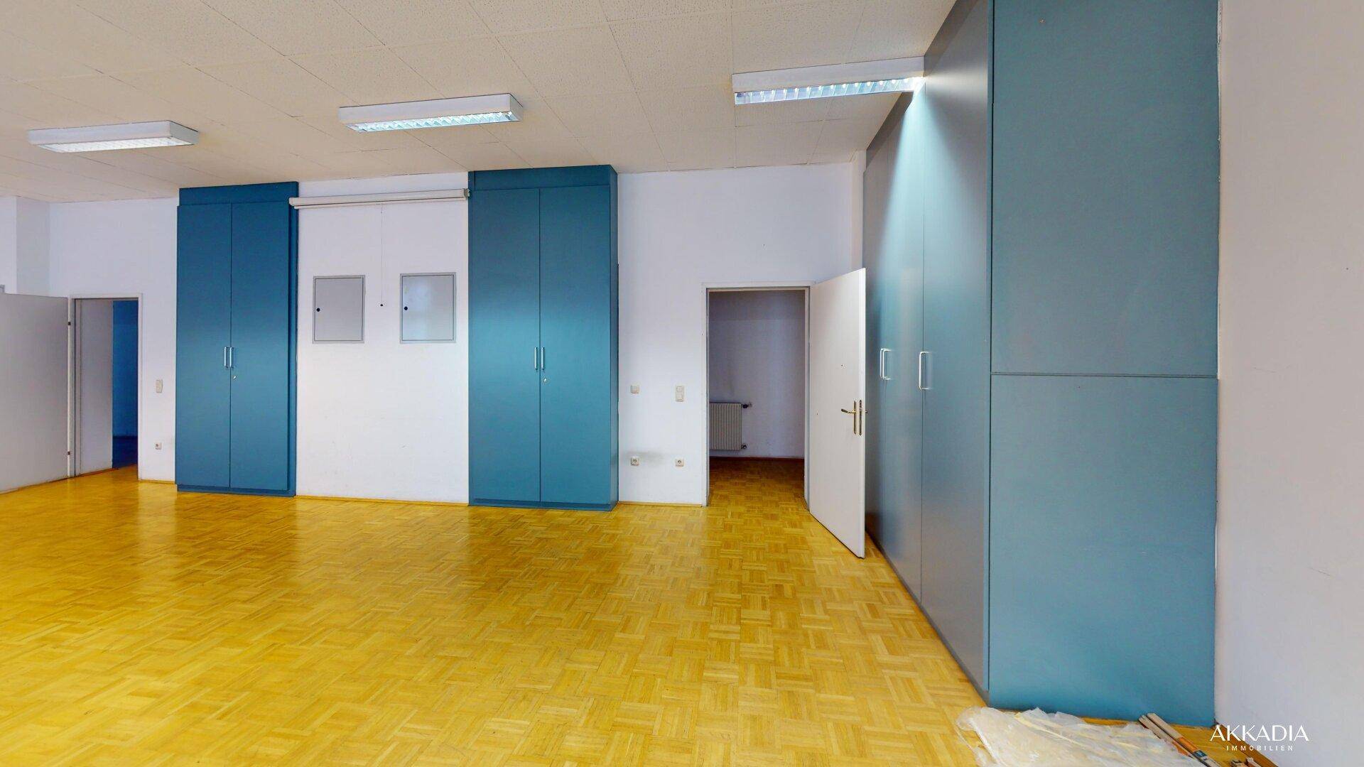 Geräumiger Raum mit Parkettboden, weißen Wänden und blauen Einbauschränken, bietet viel Stauraum.
