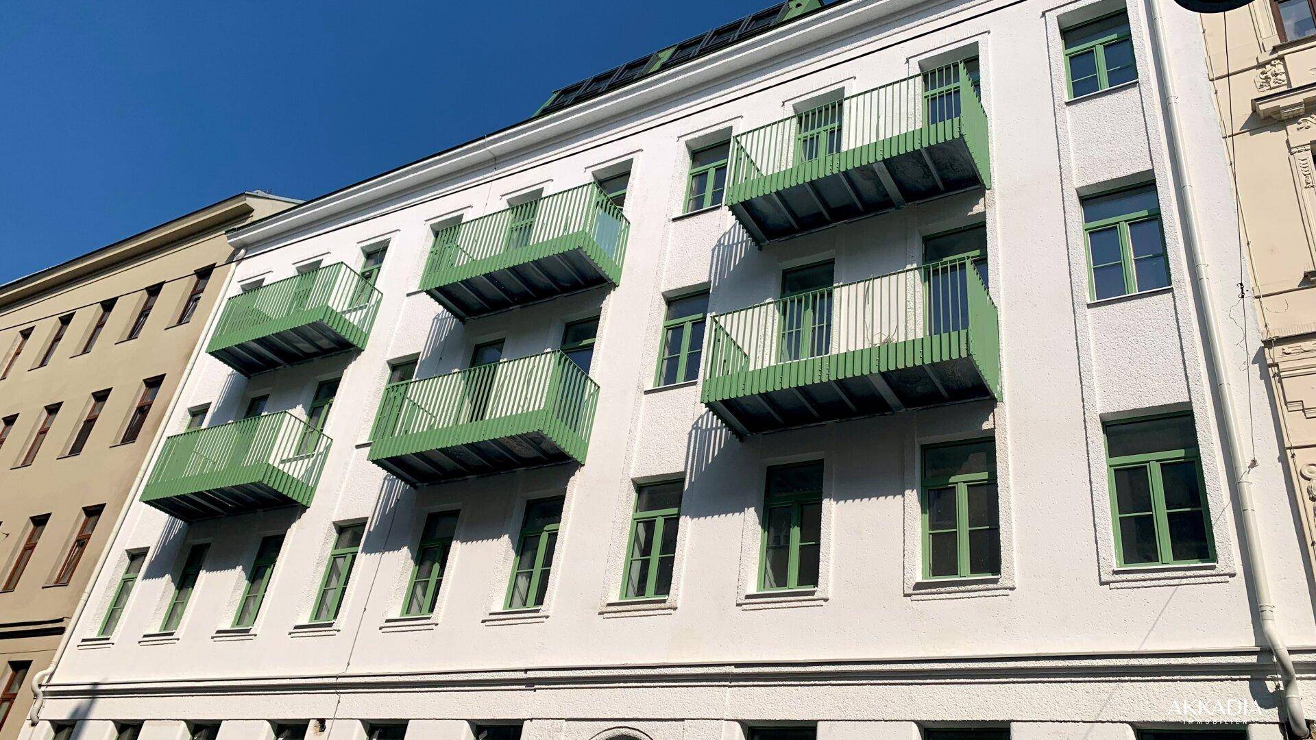 Fassade eines Wohnhauses mit markanten grünen Balkonen und hellen Fenstern bei Sonnenschein.