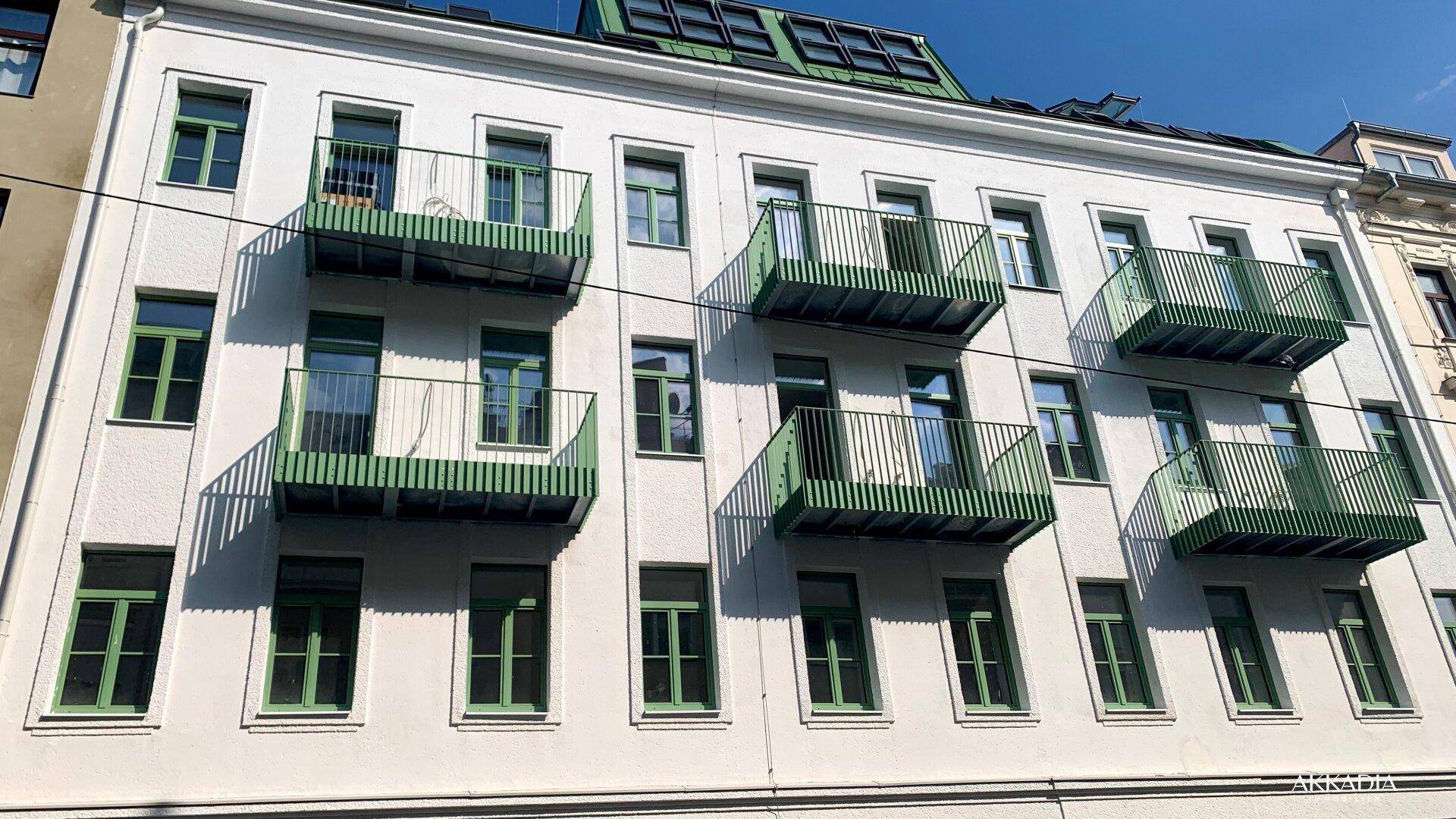 Die helle Fassade des Gebäudes wird durch die leuchtend grünen Balkone und Fensterrahmen akzentuiert.