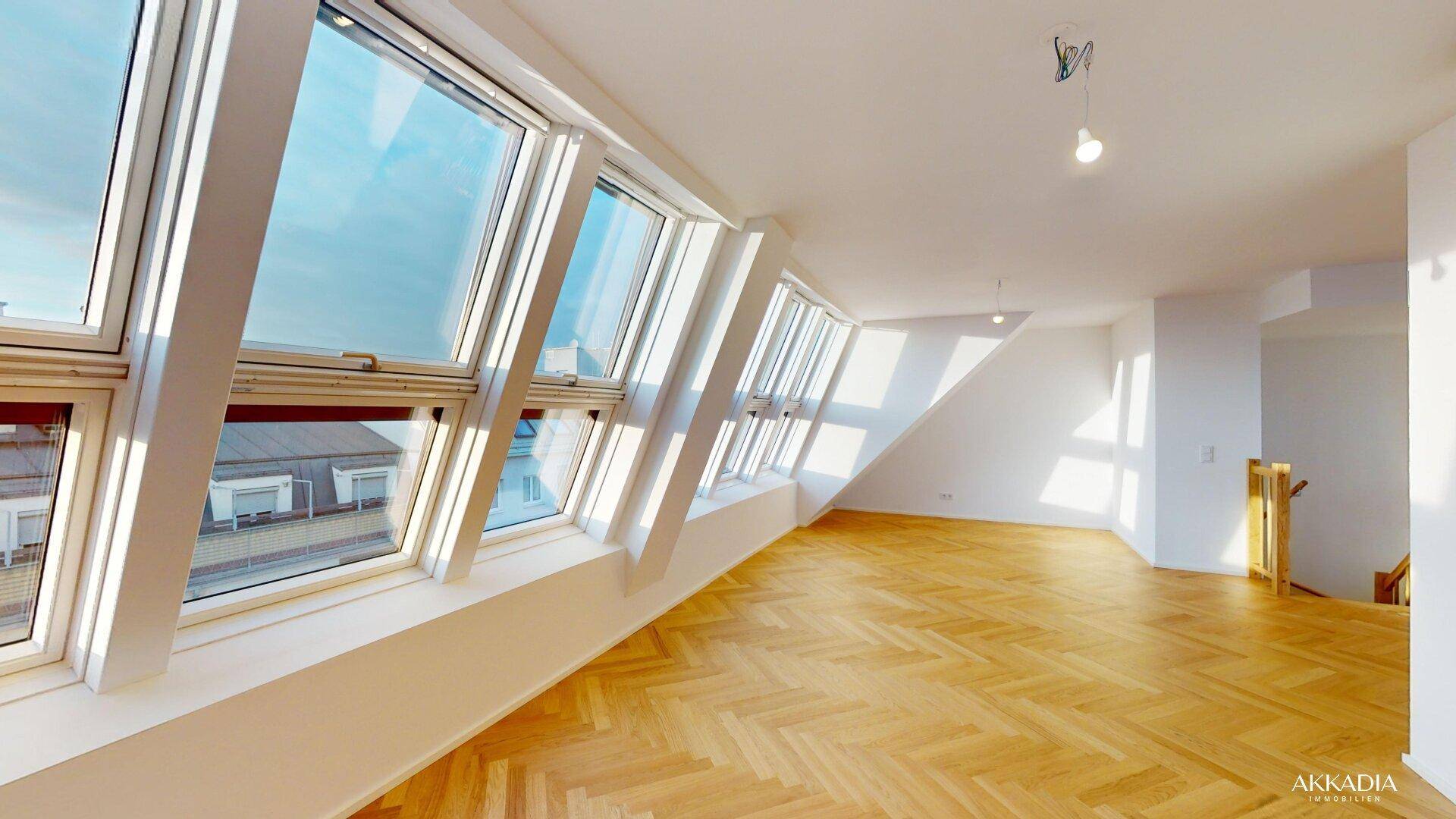 Lichtdurchfluteter Wohnraum im Dachgeschoss mit Fischgrätparkett und großen Dachfenstern.