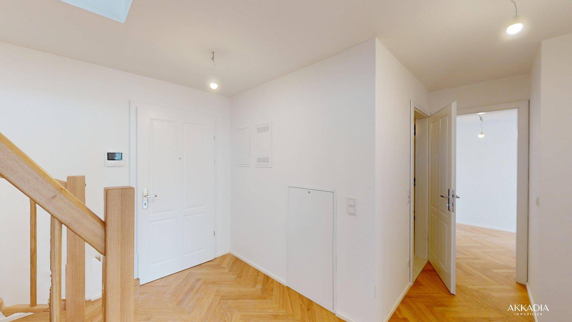 Eingangsbereich mit weißer Tür, Fischgrätparkett und einer eleganten Holztreppe.