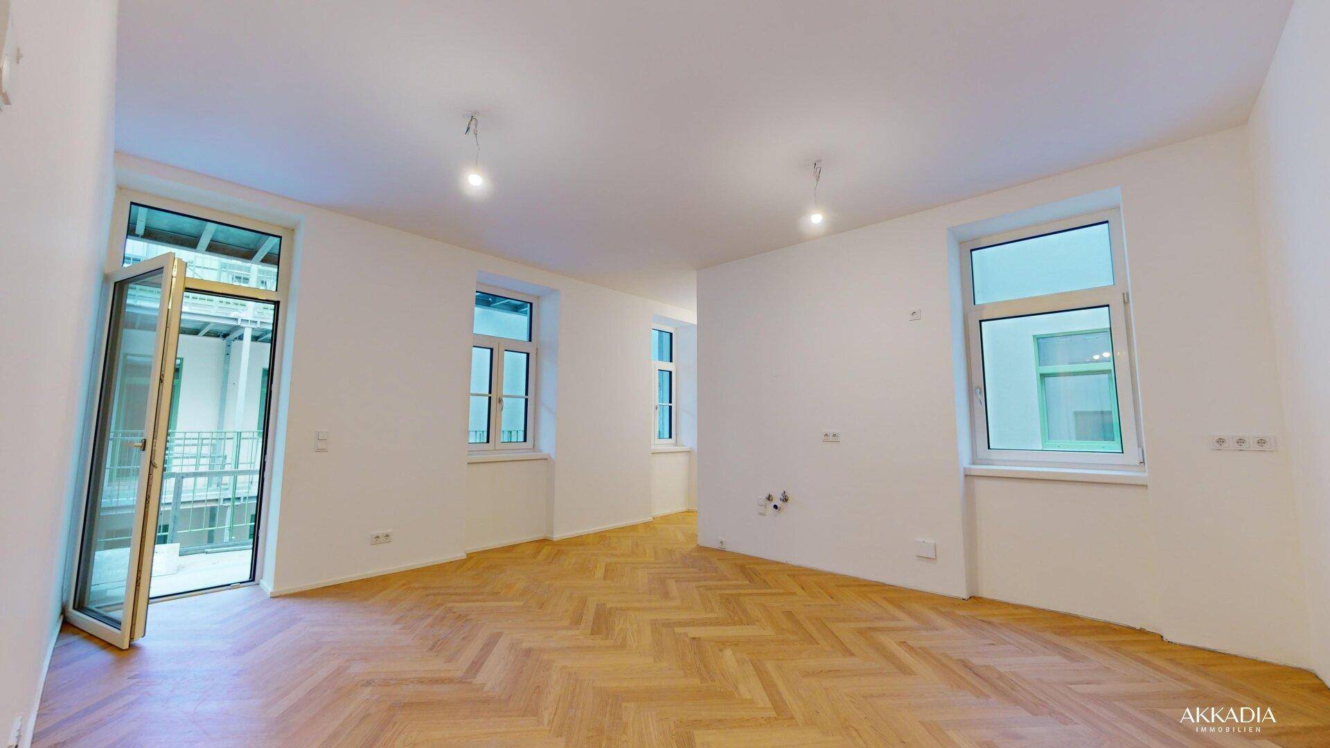 Großes, helles Zimmer mit Fischgrätparkett und mehreren Fenstern, das viel Tageslicht bietet.