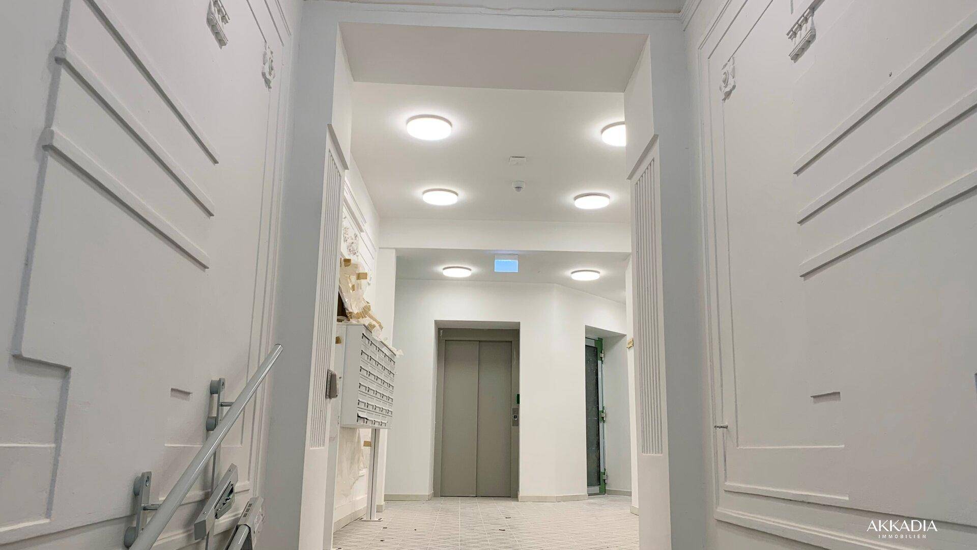 Modernisierter Eingangsbereich eines Mehrfamilienhauses mit Aufzug und dekorativen Wandpaneelen.