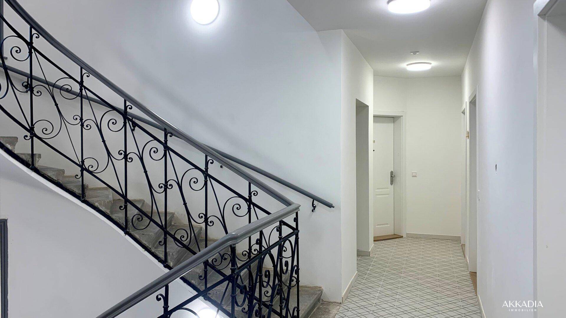Treppenhaus mit schmiedeeisernem Geländer und gefliestem Boden in einem Altbau.