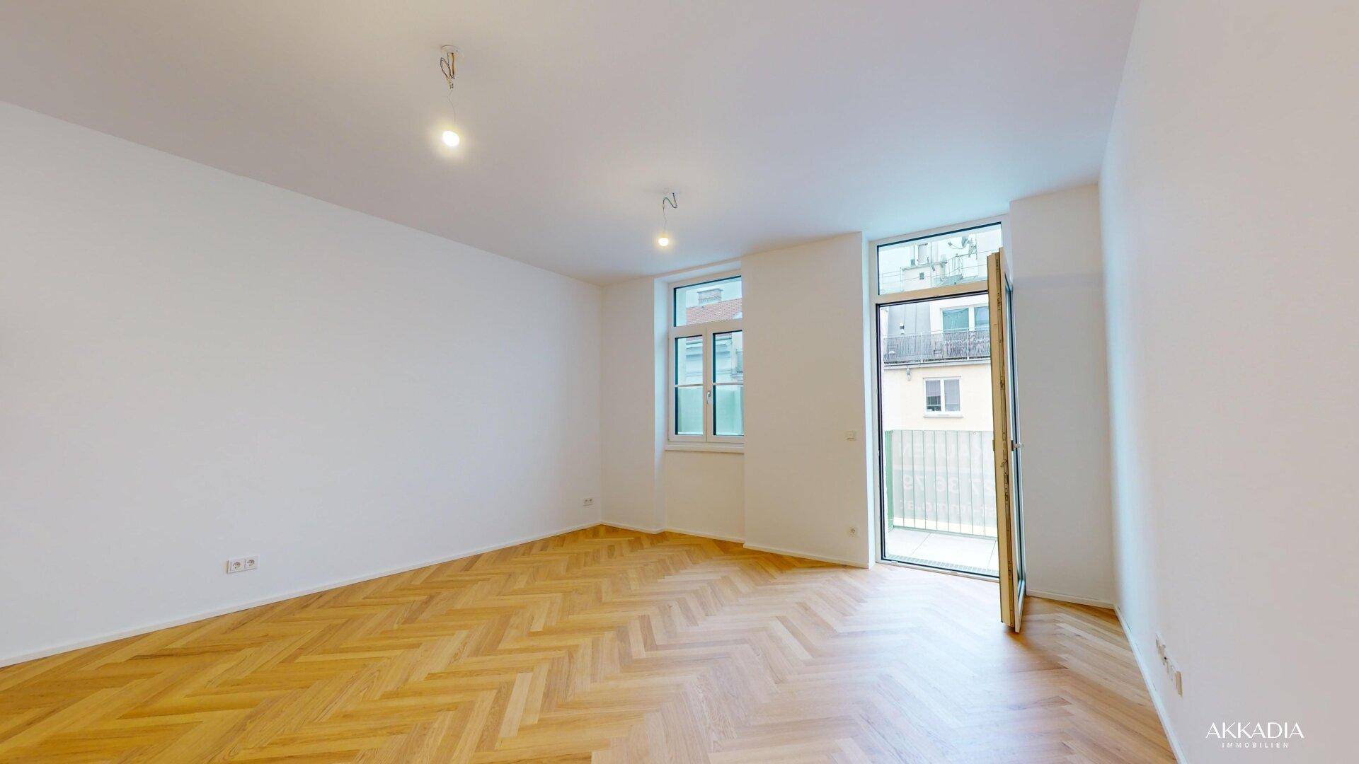 Helles, leeres Zimmer mit Fischgrätparkettboden und Zugang zu einem Balkon.