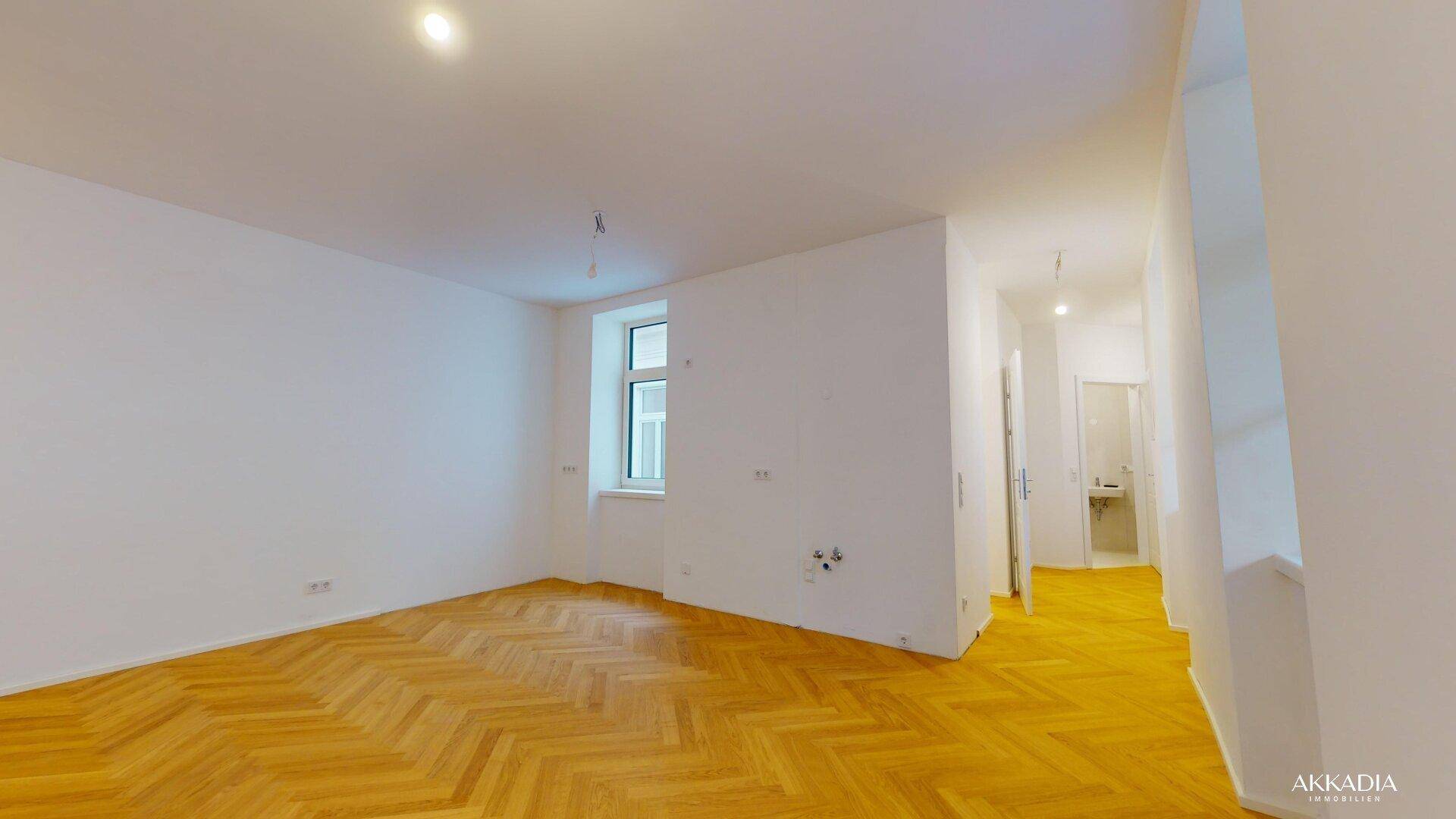 Leeres, helles Zimmer mit Fischgrätparkett und Blick in den Flur und ein weiteres Zimmer.