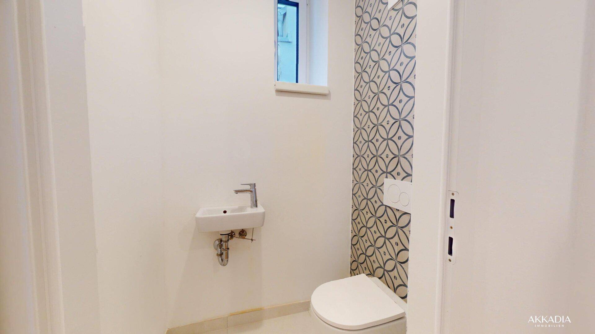 Modernes Gäste-WC mit kleinem Waschbecken, Wand-WC und dekorativen Fliesen.
