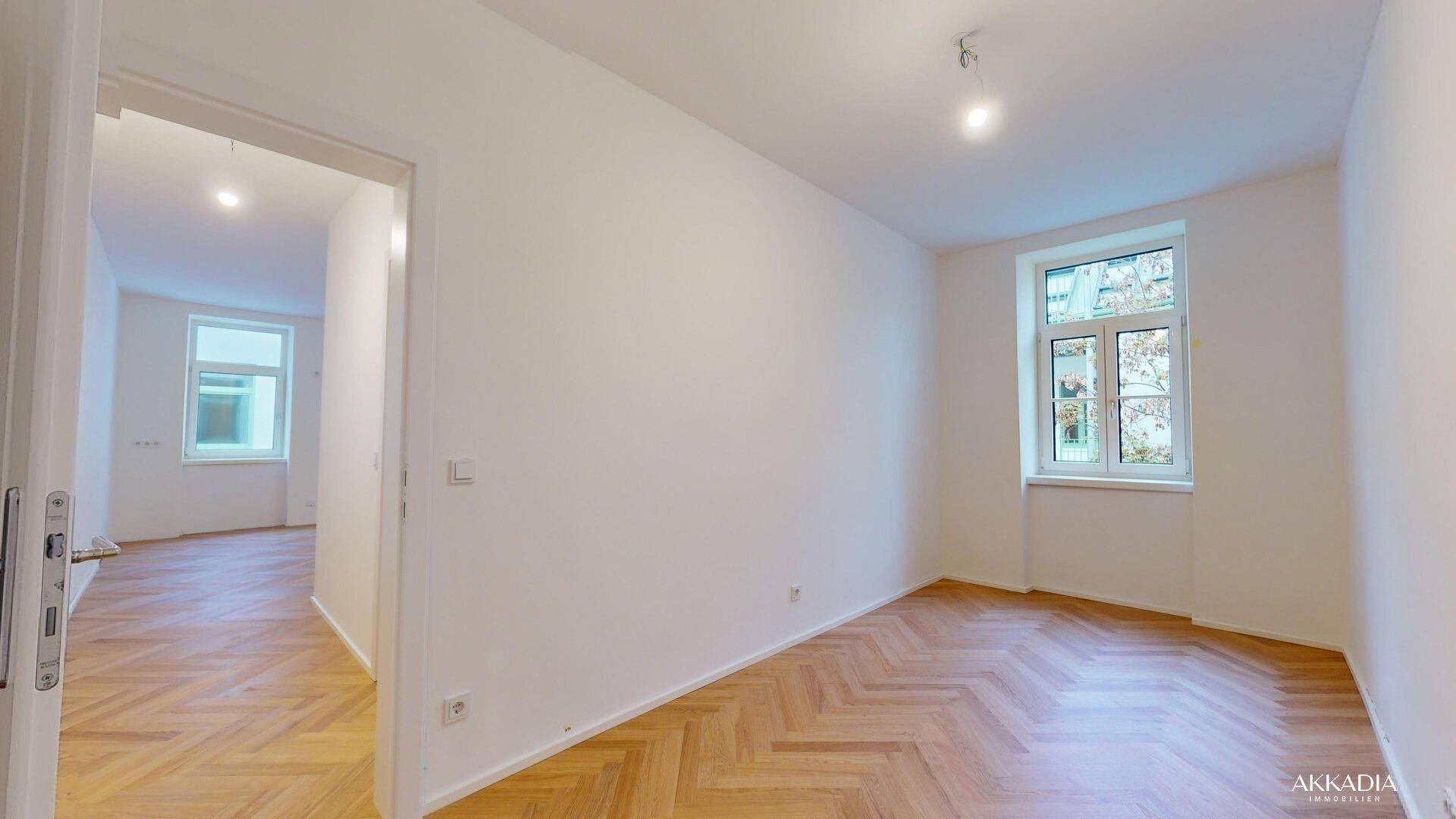 Helles, leeres Zimmer mit Fischgrätparkett und Fenster, ideal als Schlaf- oder Arbeitszimmer.