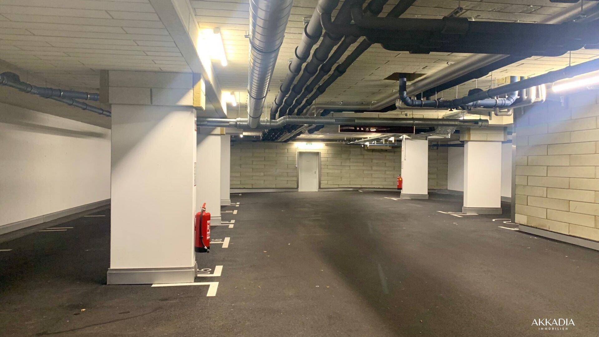 Geräumige Tiefgarage mit markierten Stellplätzen, massiver Bauweise und sichtbaren Installationen.