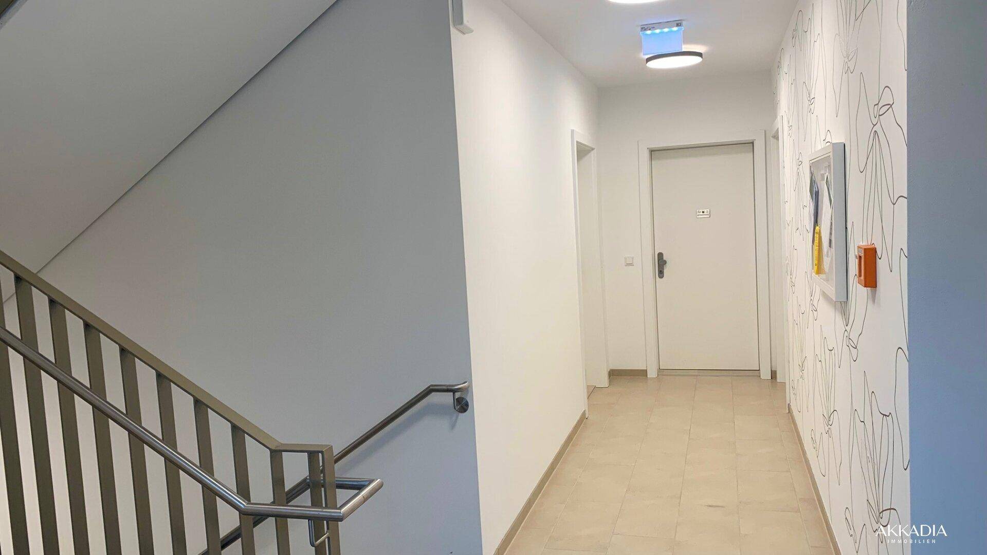 Heller Flur mit Treppenaufgang, modernem Wanddesign und Fliesenboden.