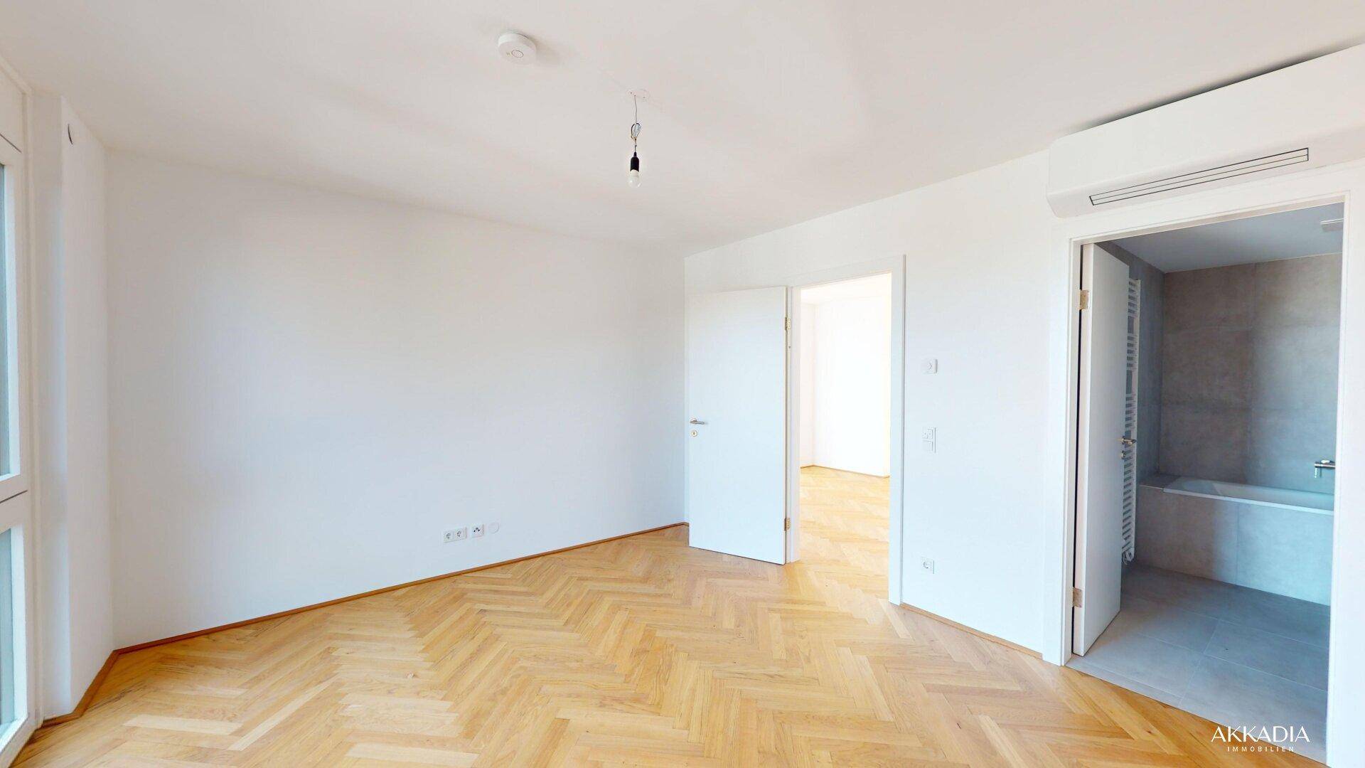 Helles Schlafzimmer mit Fischgrätparkett und direktem Zugang zu einem Badezimmer.