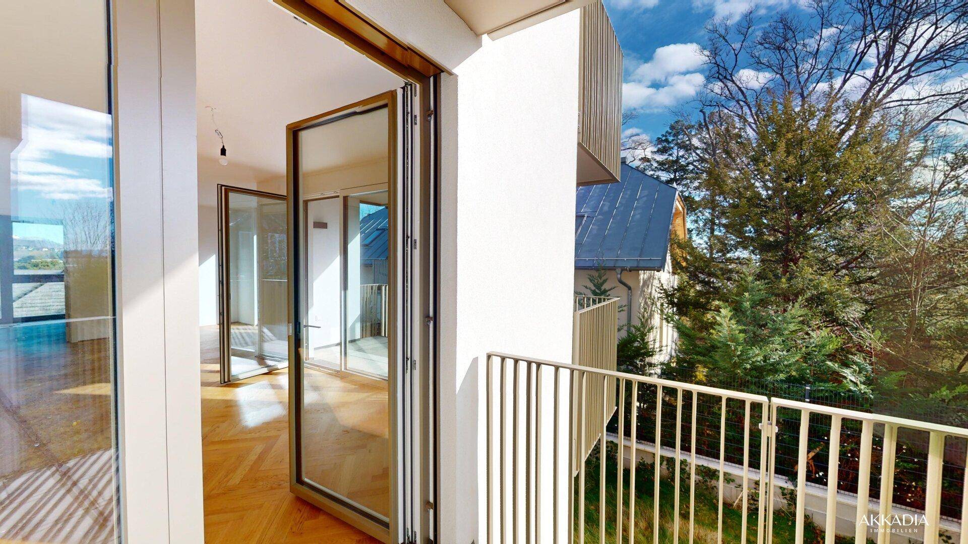 Sonniger Balkon mit Blick auf die grüne Umgebung und Zugang zu einem hellen Innenraum.