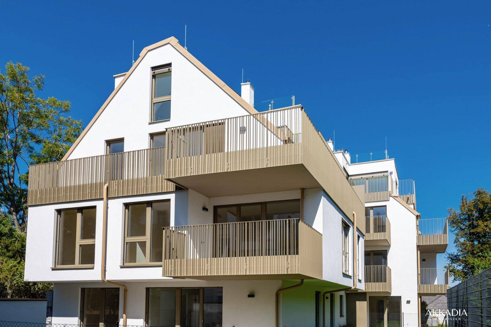 Neubau mit moderner Architektur, hellen Fassaden und großzügigen Balkonen unter blauem Himmel.