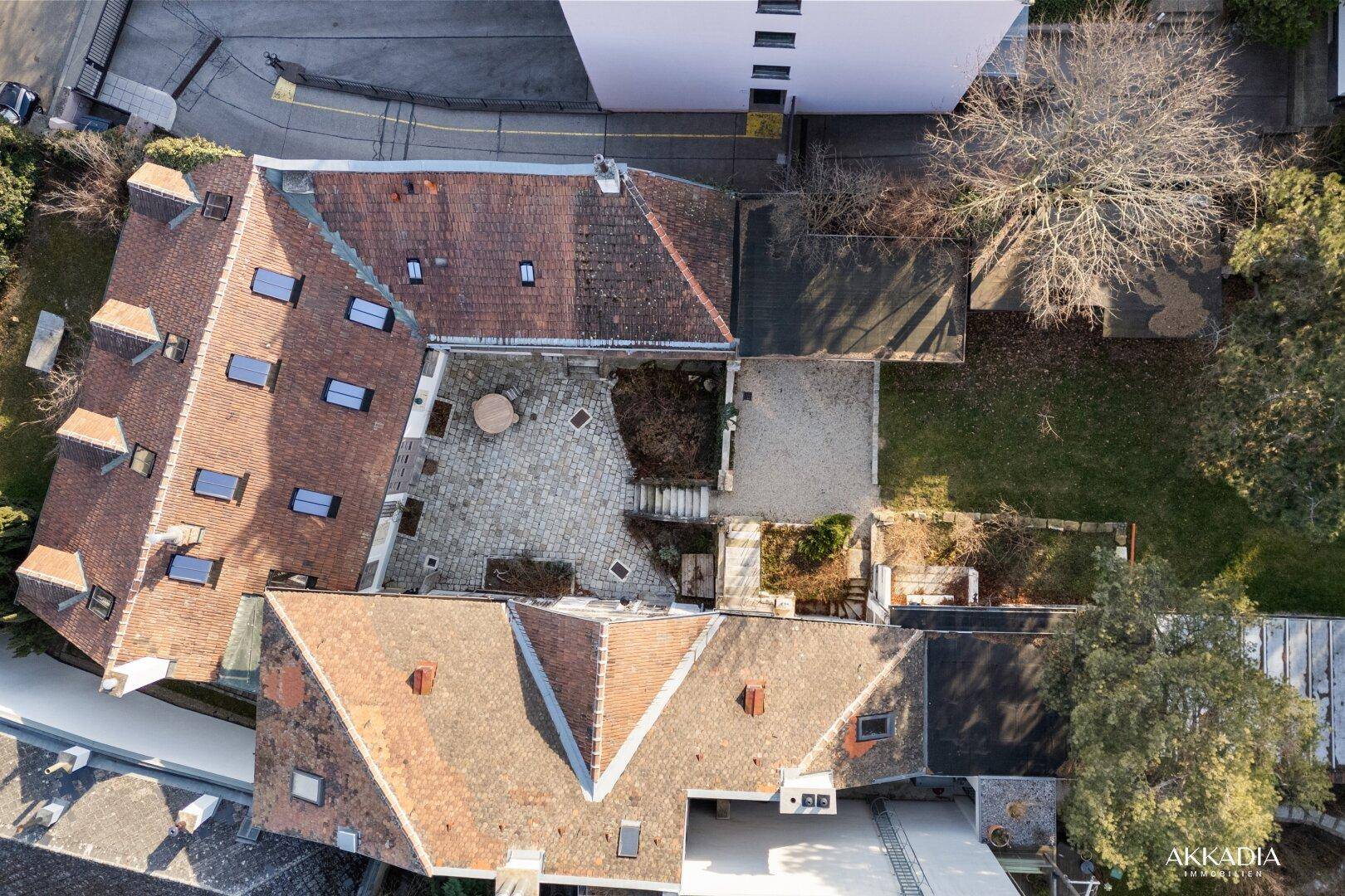 Luftaufnahme des Anwesens mit mehreren Gebäuden, Dächern und einem gepflasterten Innenhof.