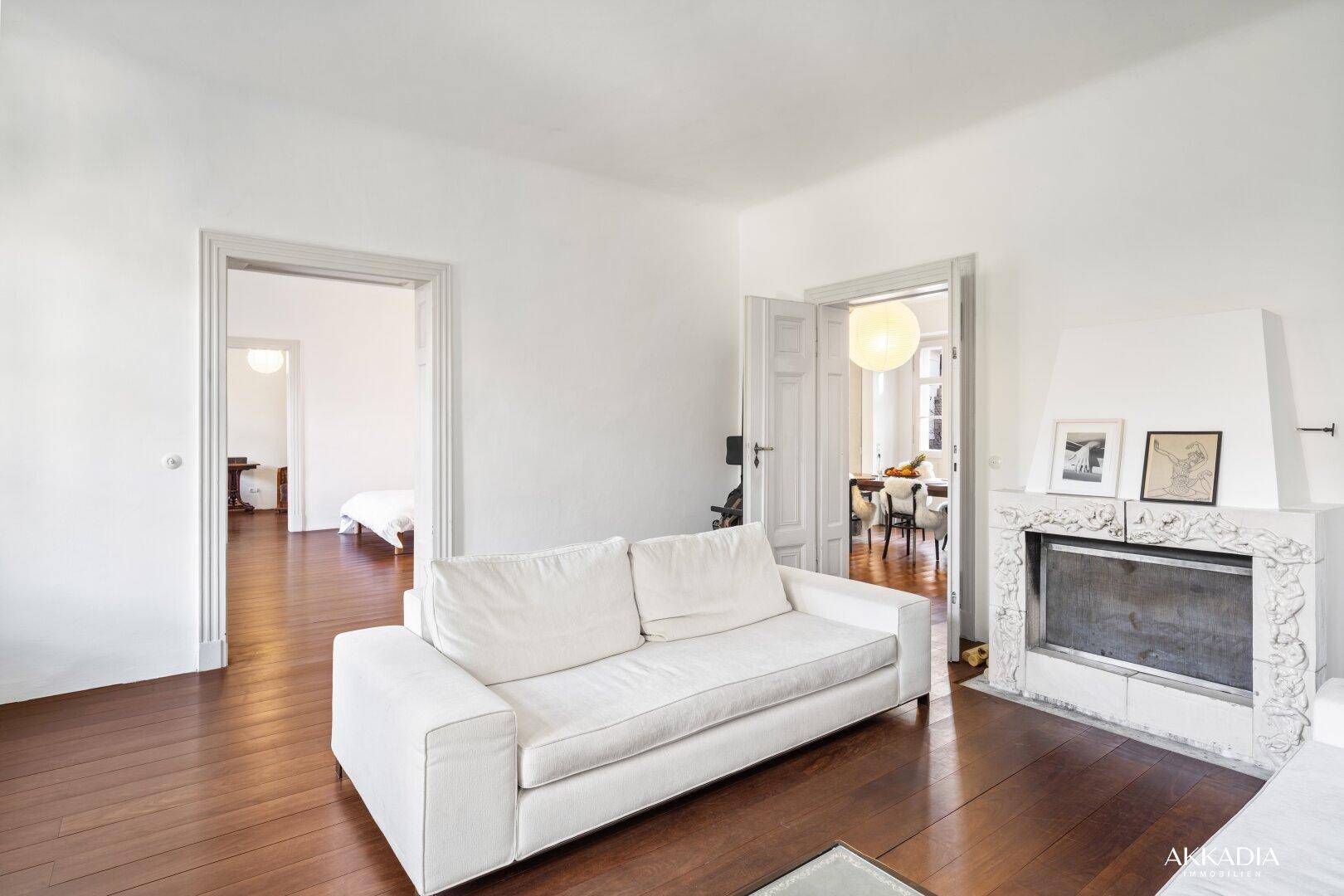 Geräumiges Wohnzimmer mit dunklem Holzboden, weißem Sofa und einem dekorativen Kamin.