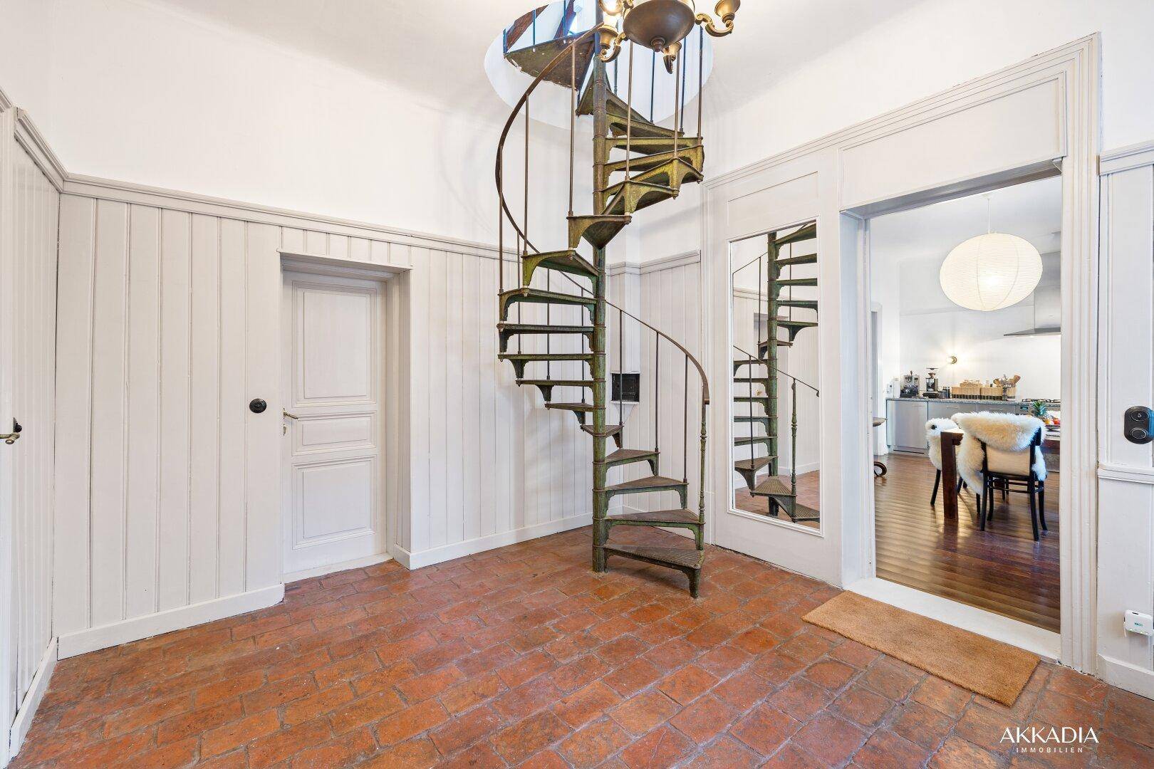 Historischer Flur mit Terrakottaboden und einer eleganten schmiedeeisernen Wendeltreppe.