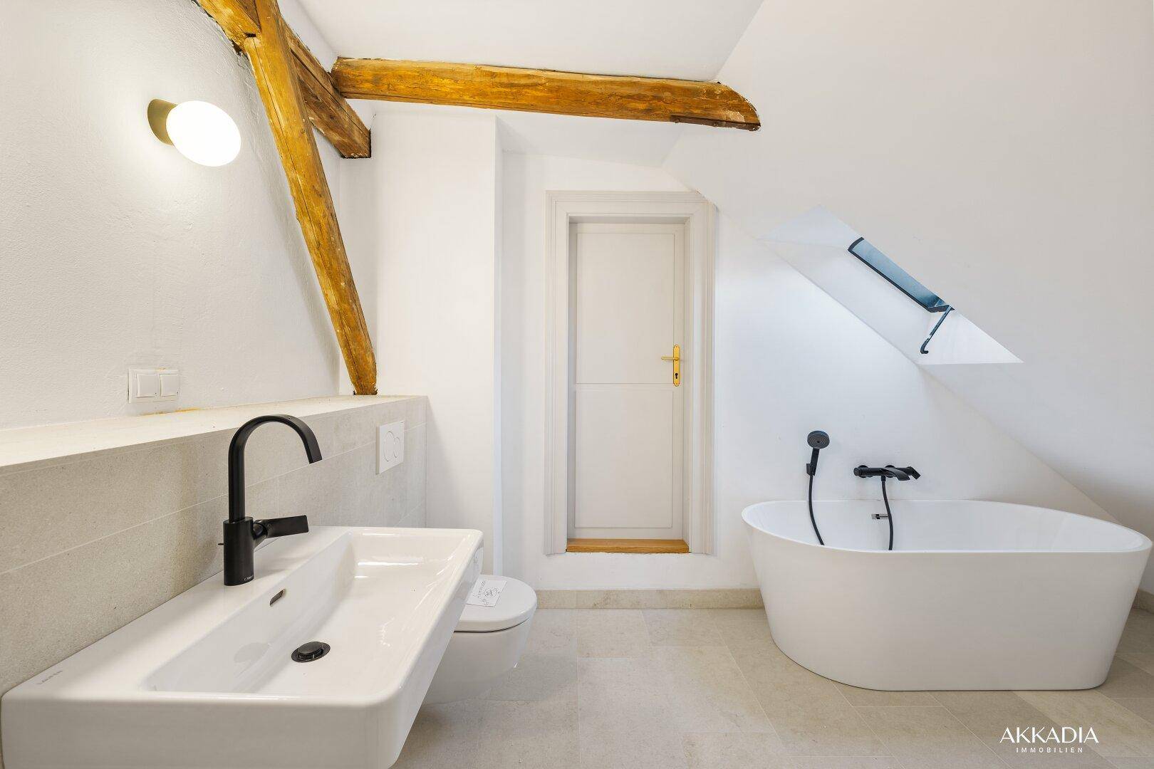 Modernes Badezimmer im Dachgeschoss mit freistehender Badewanne, Waschtisch und Dachfenster.