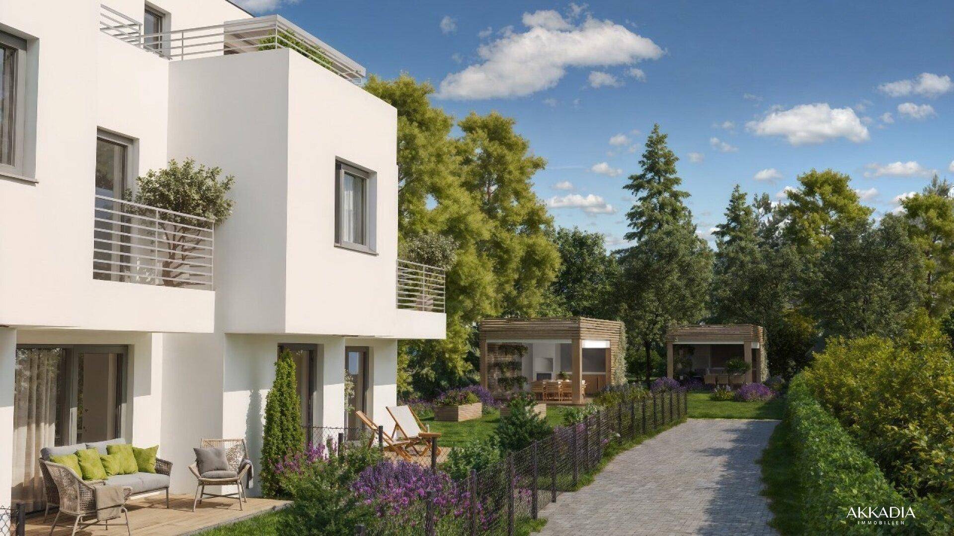 Seitlicher Blick auf die moderne Wohnanlage mit gepflegtem Garten, Sitzgelegenheiten und einem Weg.