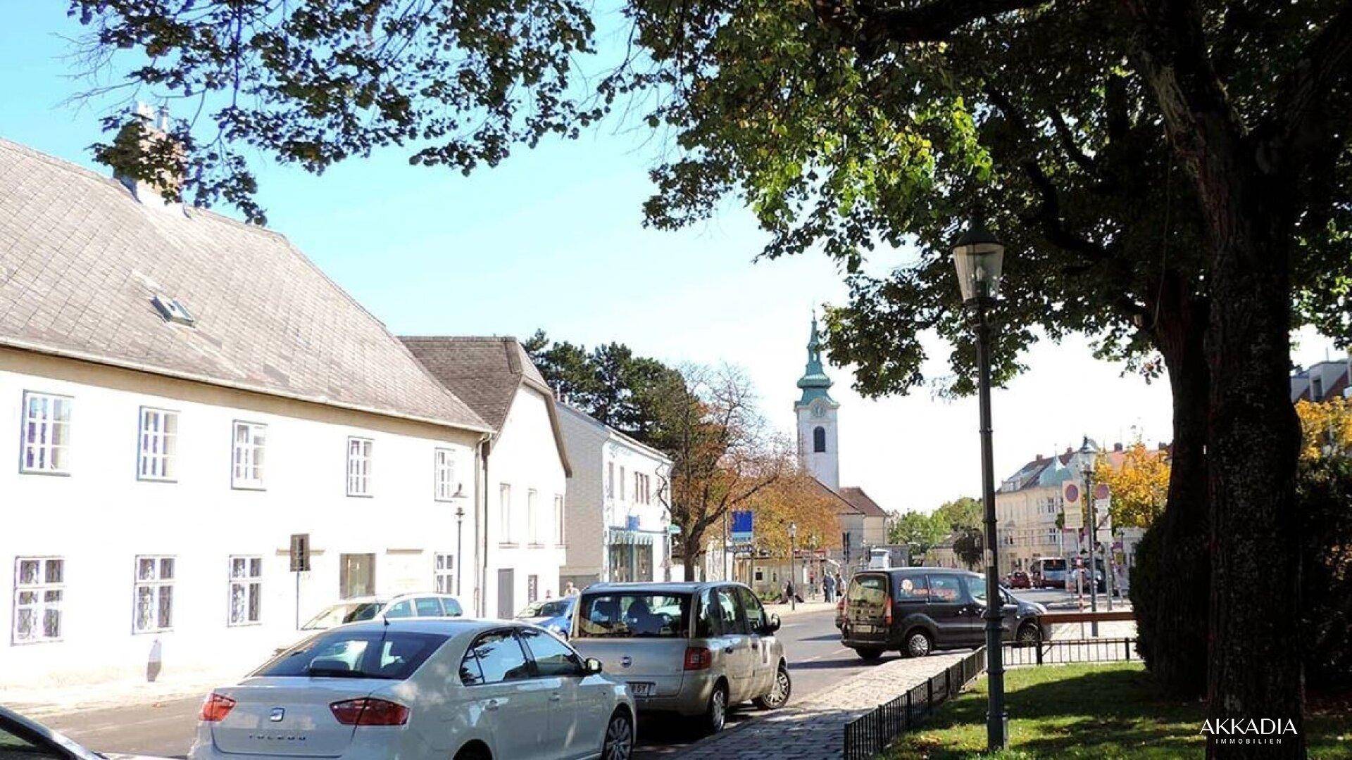 Blick auf eine belebte Straße mit parkenden Autos, historischen Gebäuden und einer Kirche im Hintergrund.