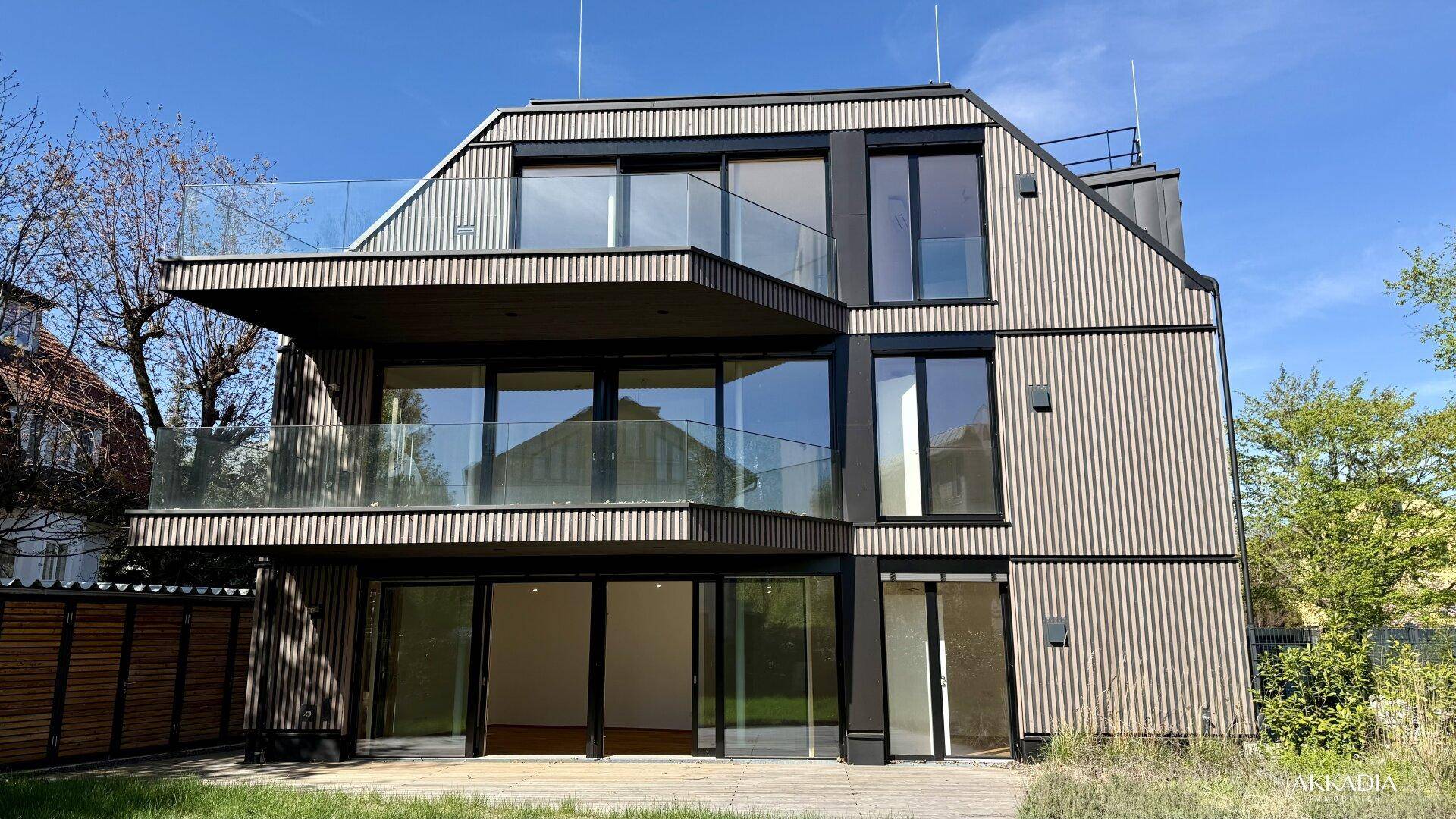 Rückansicht eines modernen Neubaus mit Holzfassade, großen Glasflächen und mehreren Balkonen.