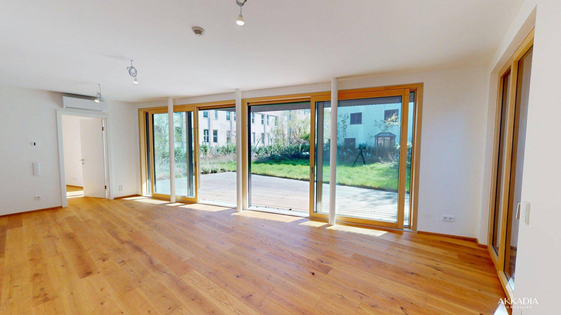Heller Wohnbereich mit Holzboden und großen Glasschiebetüren, die auf eine Holzterrasse führen.