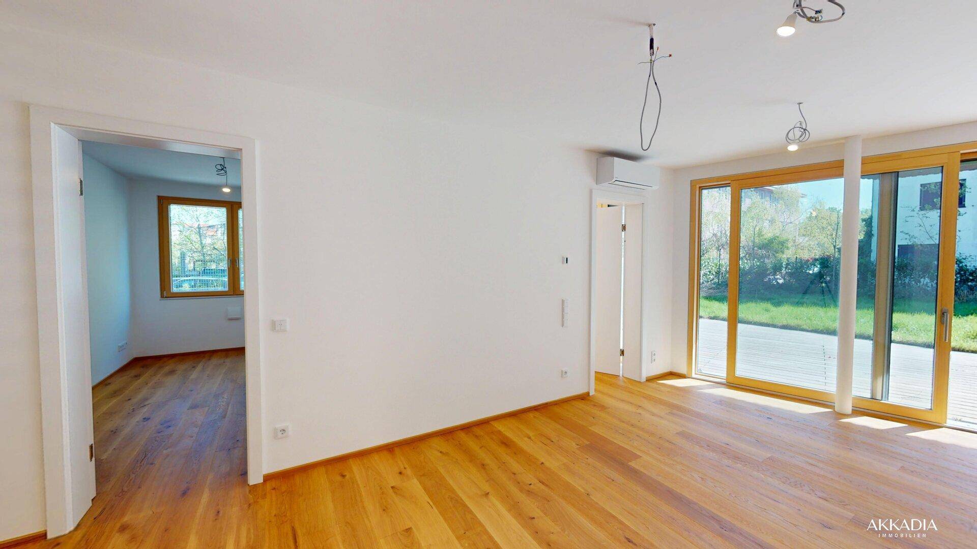 Heller Wohnbereich mit Holzboden und Zugang zu einem weiteren Zimmer, ausgestattet mit Klimaanlage.