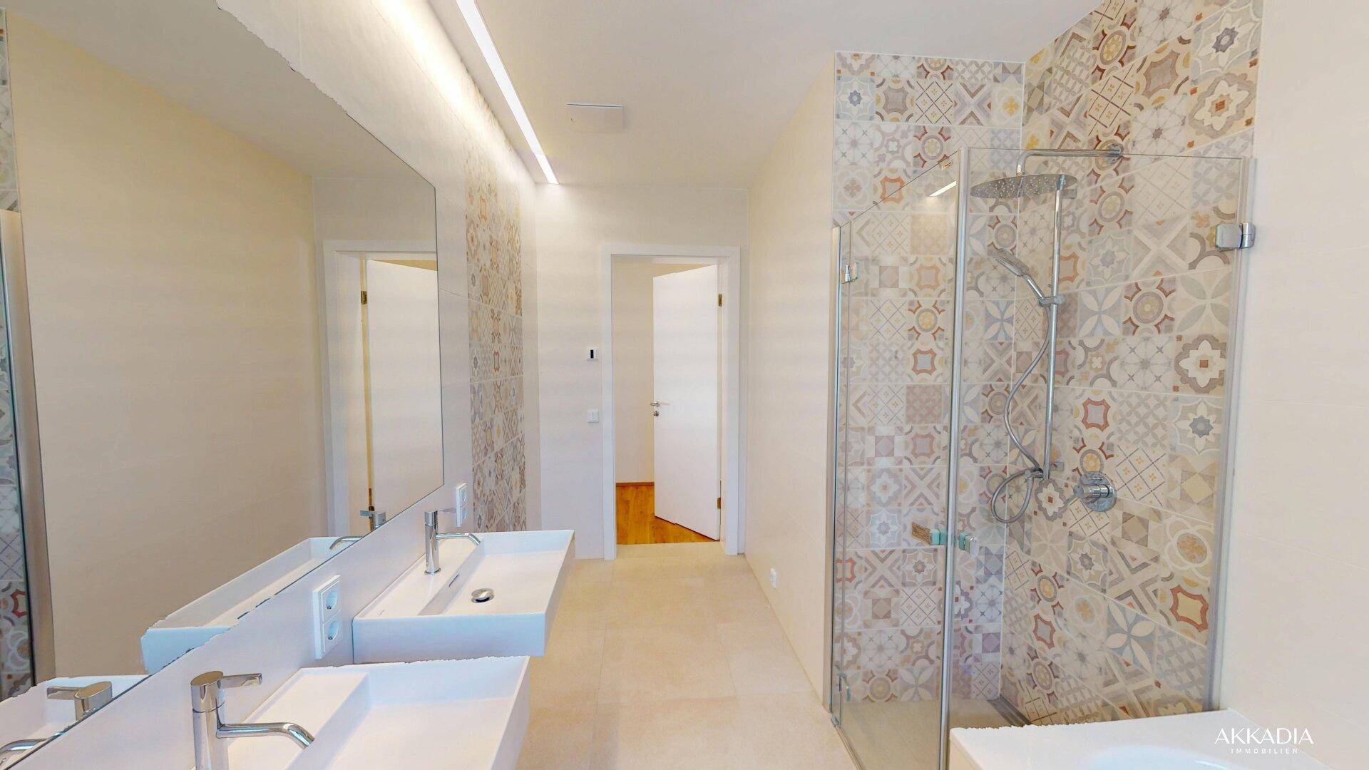 Modernes Badezimmer mit Doppelwaschbecken, begehbarer Dusche und dekorativen Fliesen an der Wand.