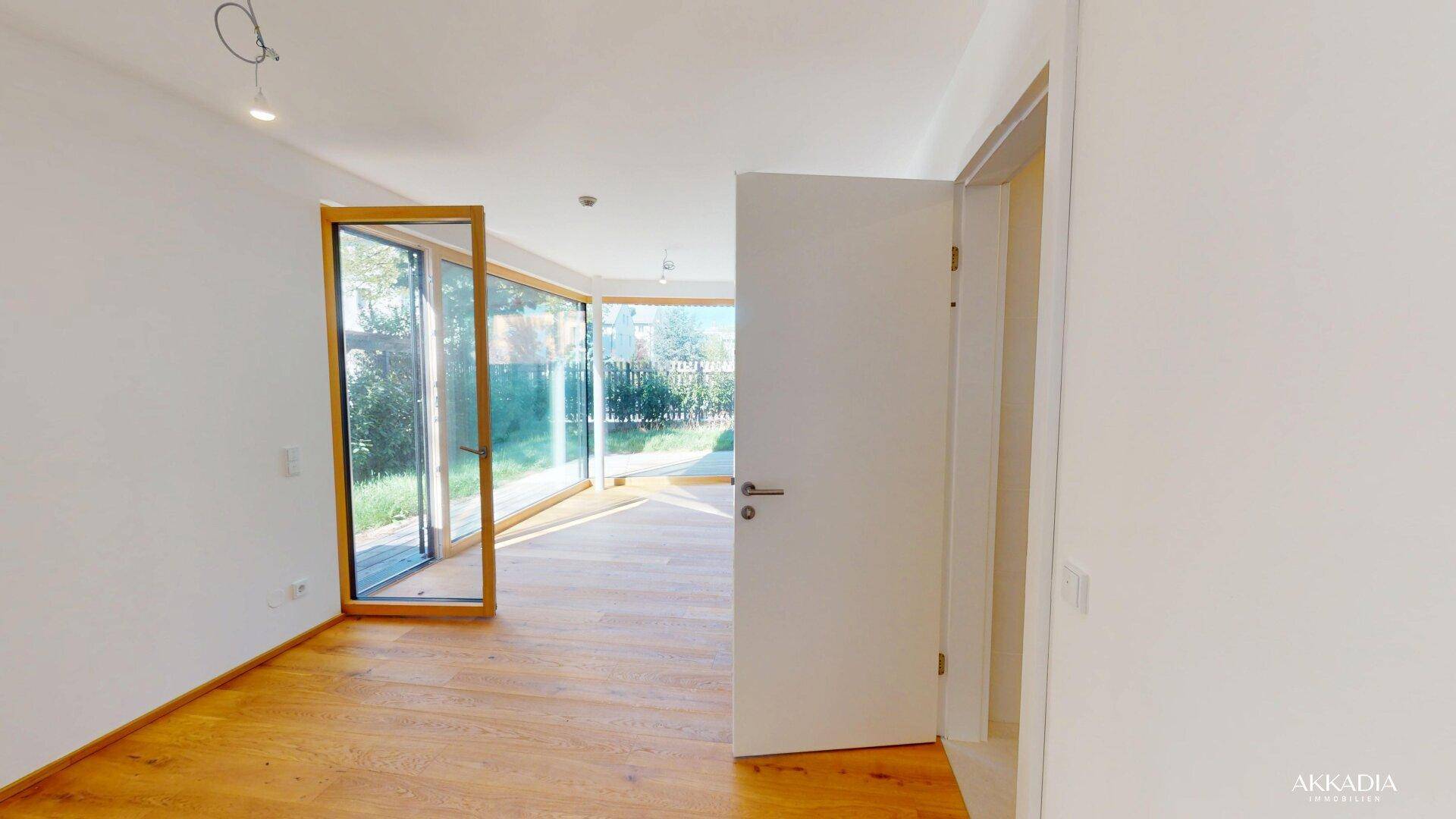 Geräumiger Wohnraum mit Holzboden und großen Fenstern, die viel Tageslicht hereinlassen.
