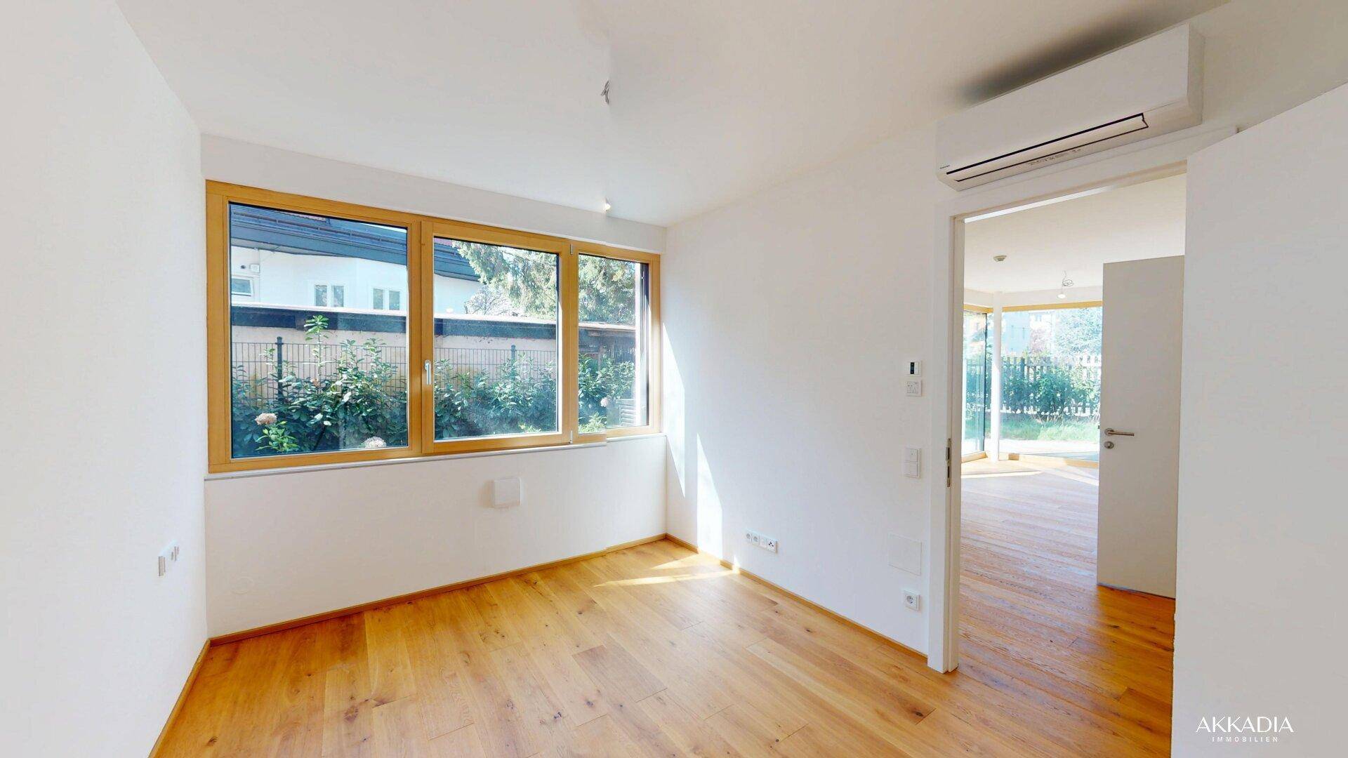 Helles Schlafzimmer mit Holzboden, großem Fenster und Blick ins Grüne.