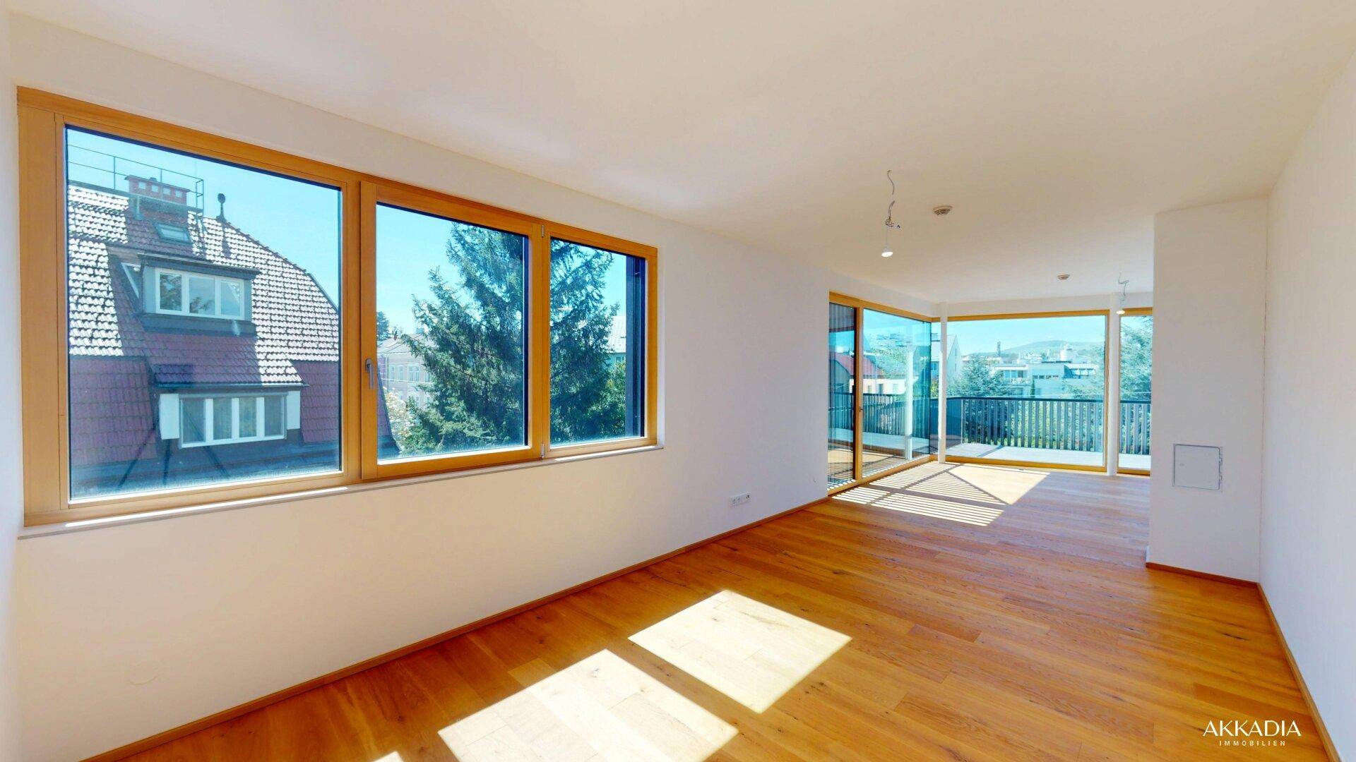 Helles Wohnzimmer mit Holzboden und großen Fenstern, die viel Sonnenlicht hereinlassen.